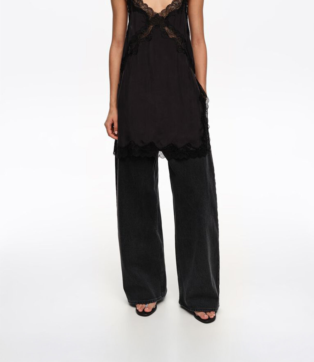 אישה לובשת גופיית תחרה שחורה ומכנסי ג'ינס רחבים, צילום אופנה על רקע לבן