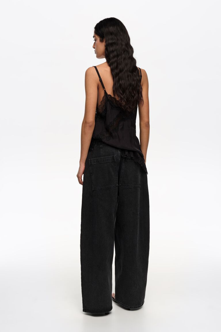 אישה לובשת גופיית תחרה שחורה ומכנסי ג'ינס שחורים רחבים, מצולמת מאחור על רקע לבן