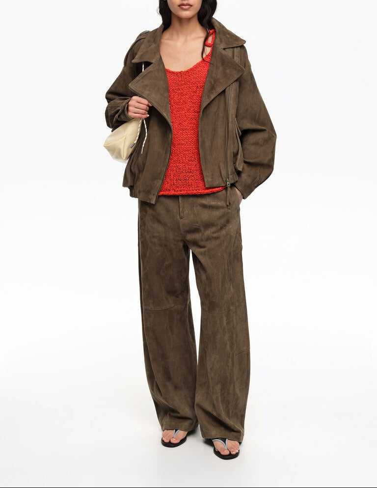 אישה בלבוש אופנתי, ז'קט ומכנסיים חומים, גופיה אדומה ותיק יד בהיר על רקע לבן