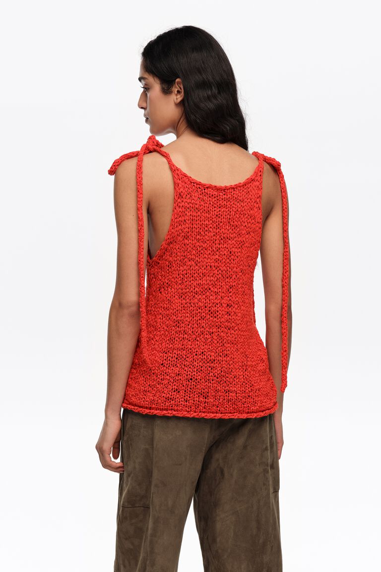 אישה לובשת גופיית סרוגה אדומה עם כתפיות קשירה ומכנסיים חומים, מצולמת מאחור, אופנת קיץ נשים