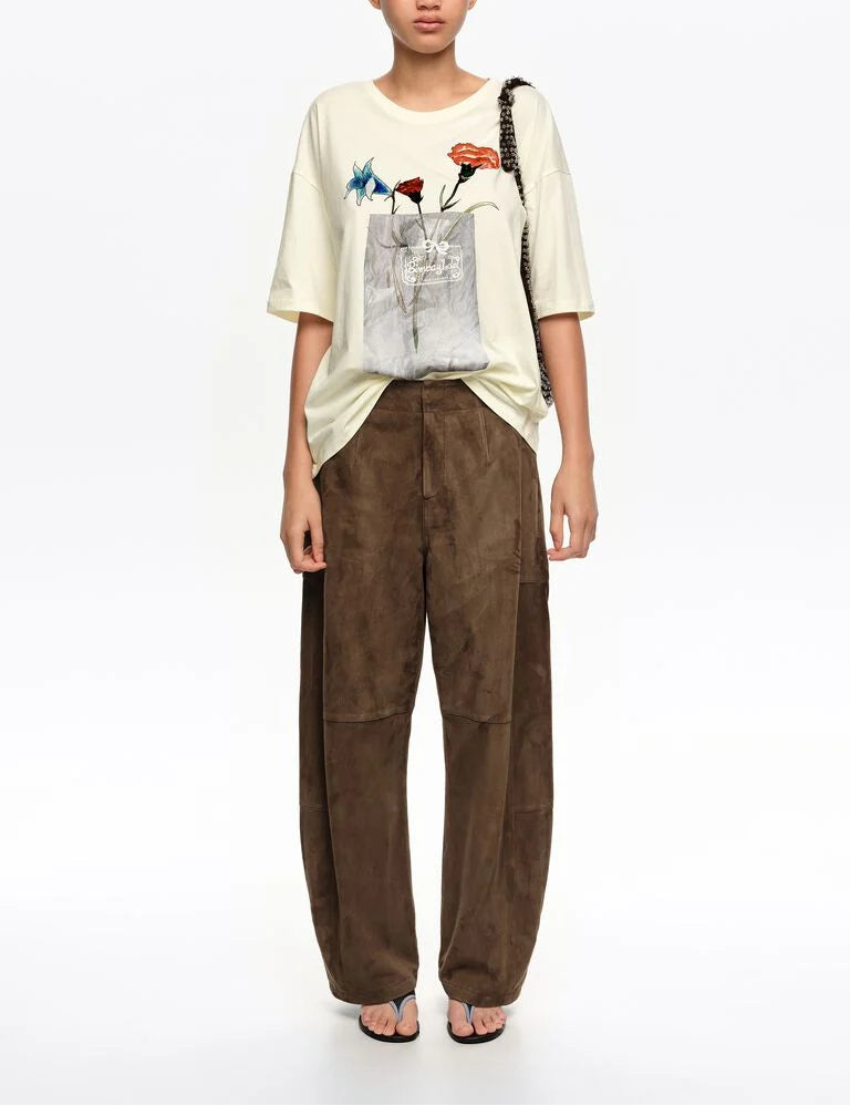 אישה לובשת טי שירט בהירה עם הדפס פרחים וכיס, מכנסיים חומים רחבים, כפכפים