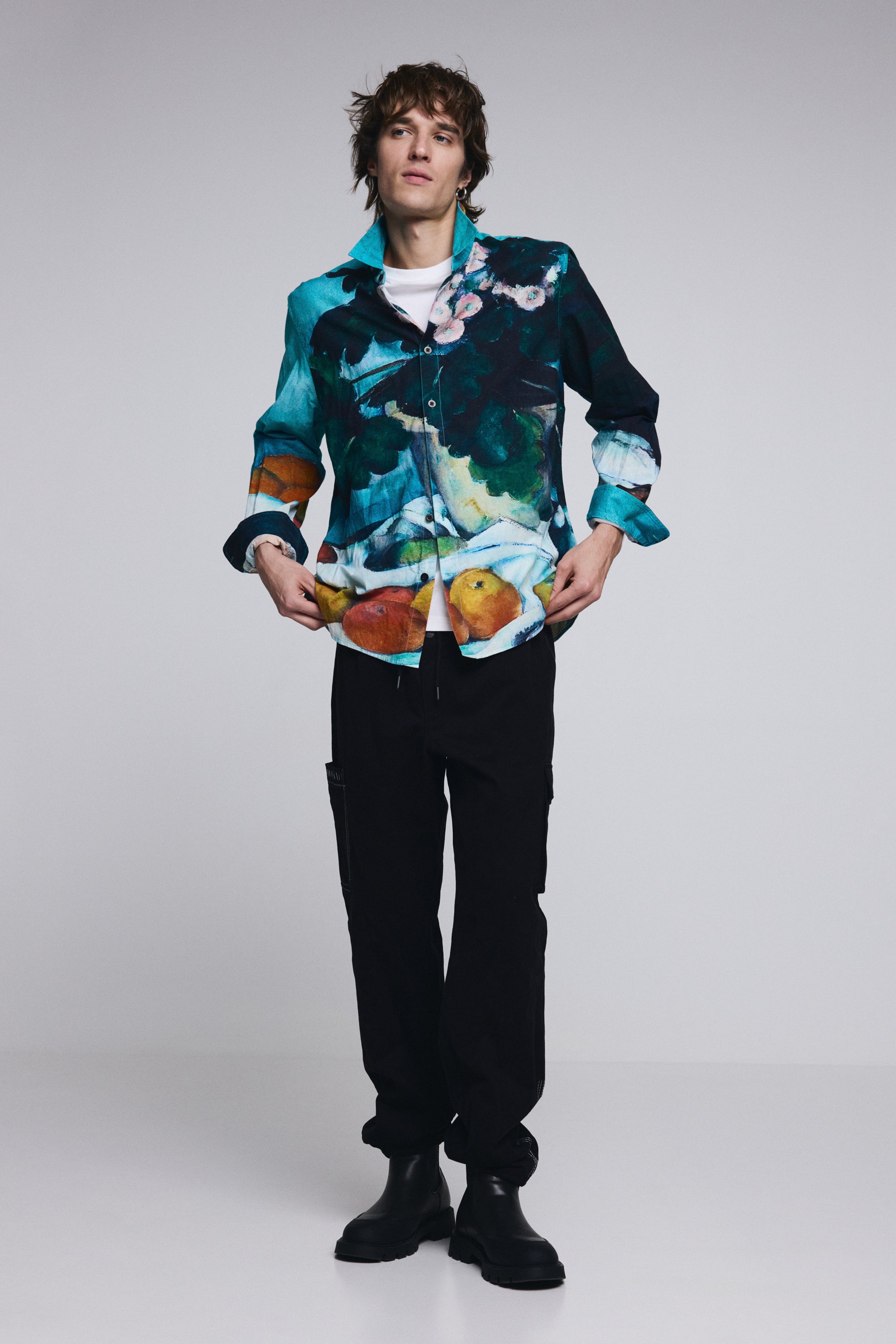 דוגמן לובש חולצה מכופתרת עם הדפס צבעוני של טבע דומם, מכנסיים שחורים ומגפיים שחורים, סטודיו