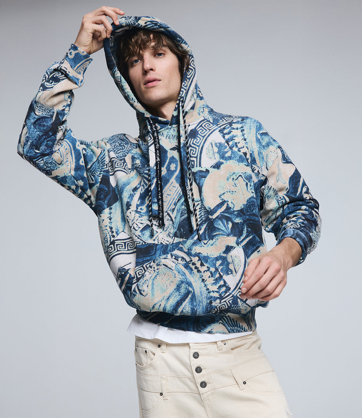 גבר לובש סווטשירט קפוצ'ון בהדפס כחול-קרם גיאומטרי ומכנסי ג'ינס בהירים, אופנת רחוב צעירה