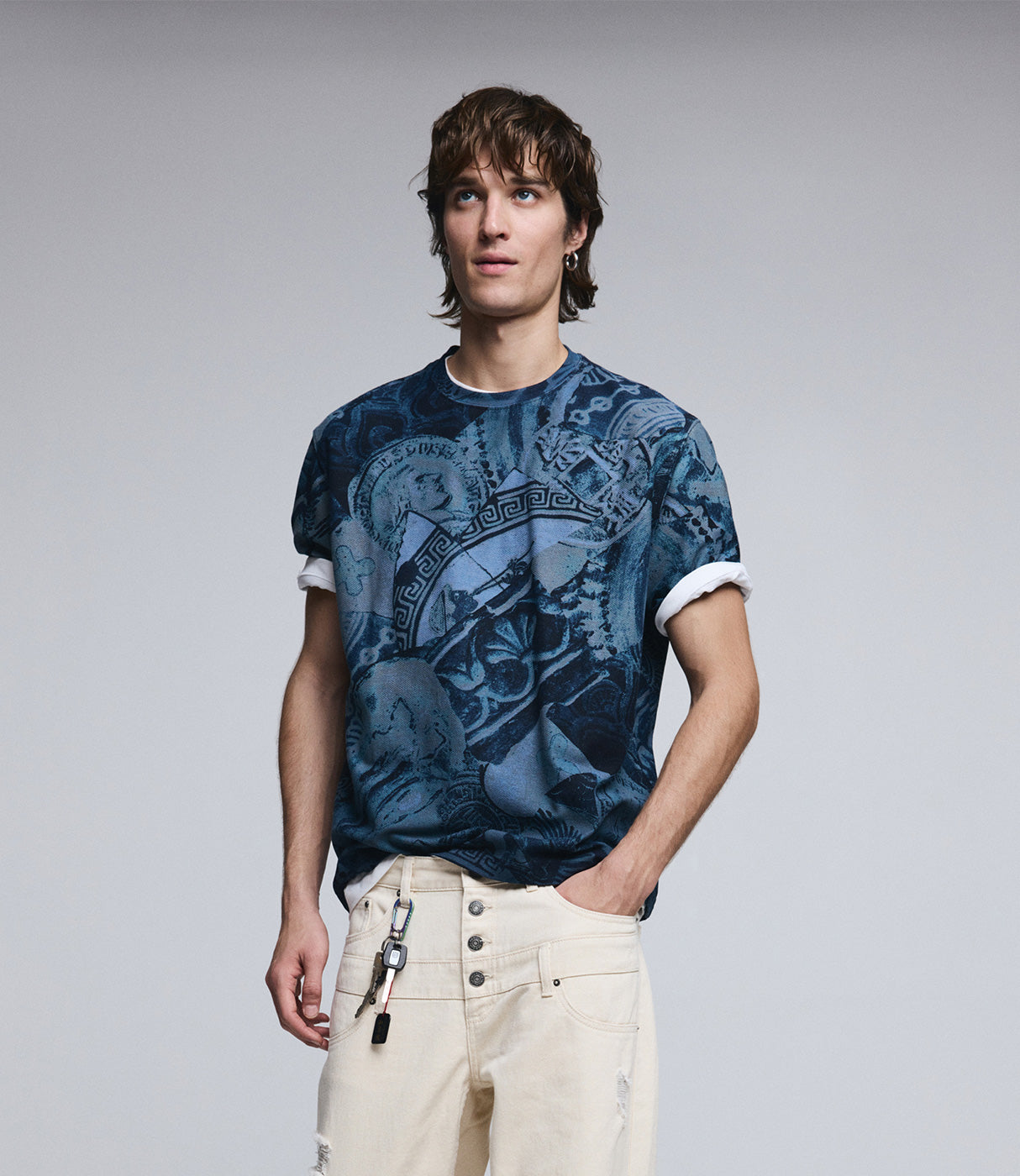 גבר לובש חולצת טריקו כחולה מודפסת דגם מודרני עם מכנס ג'ינס בגוון שמנת, צילום על רקע נייטרלי