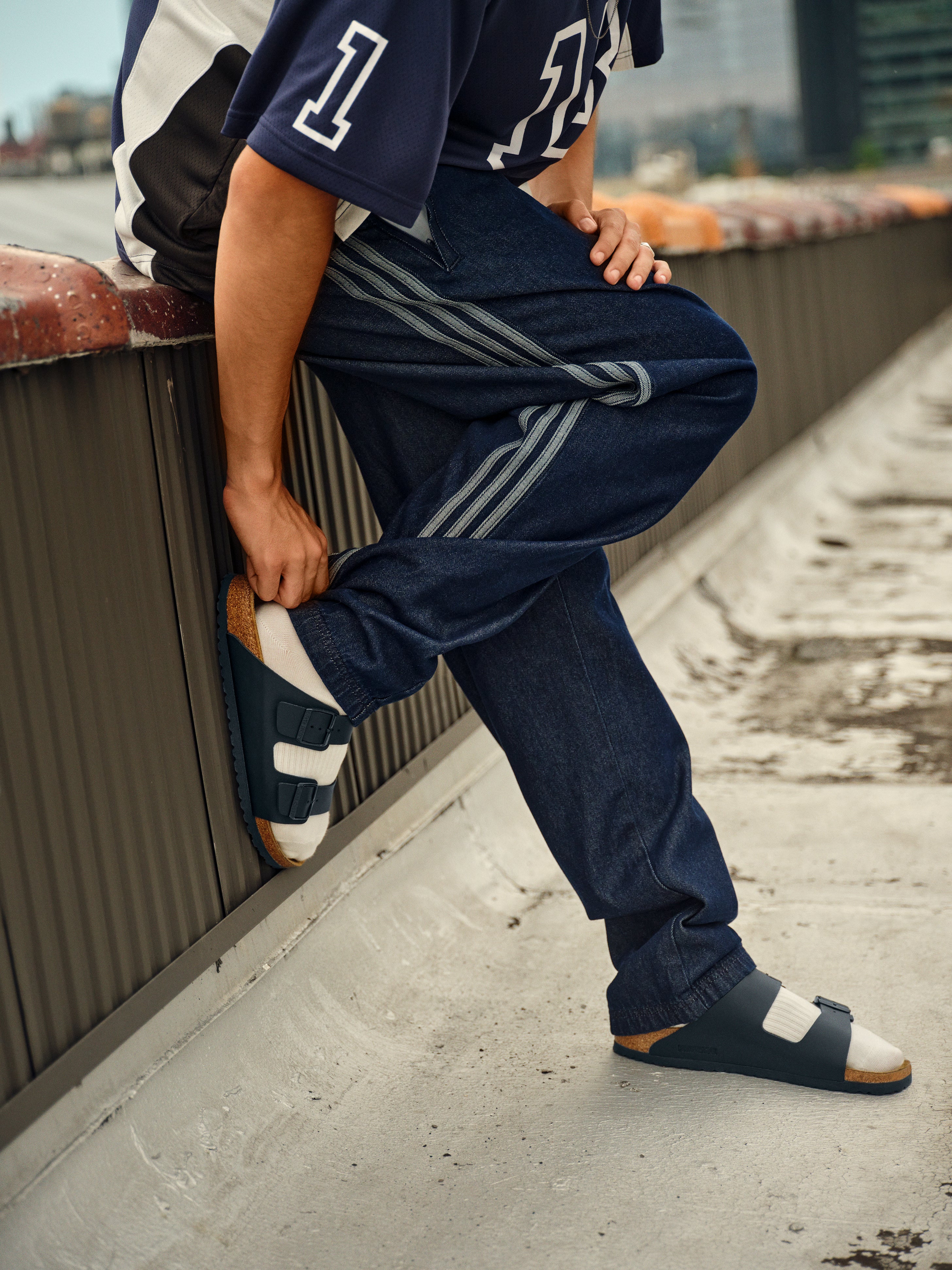 אופנת רחוב צעירה עם מכנסי ג'ינס, חולצת ספורט וכפכפי מעצבים CHOZEN על גג עירוני