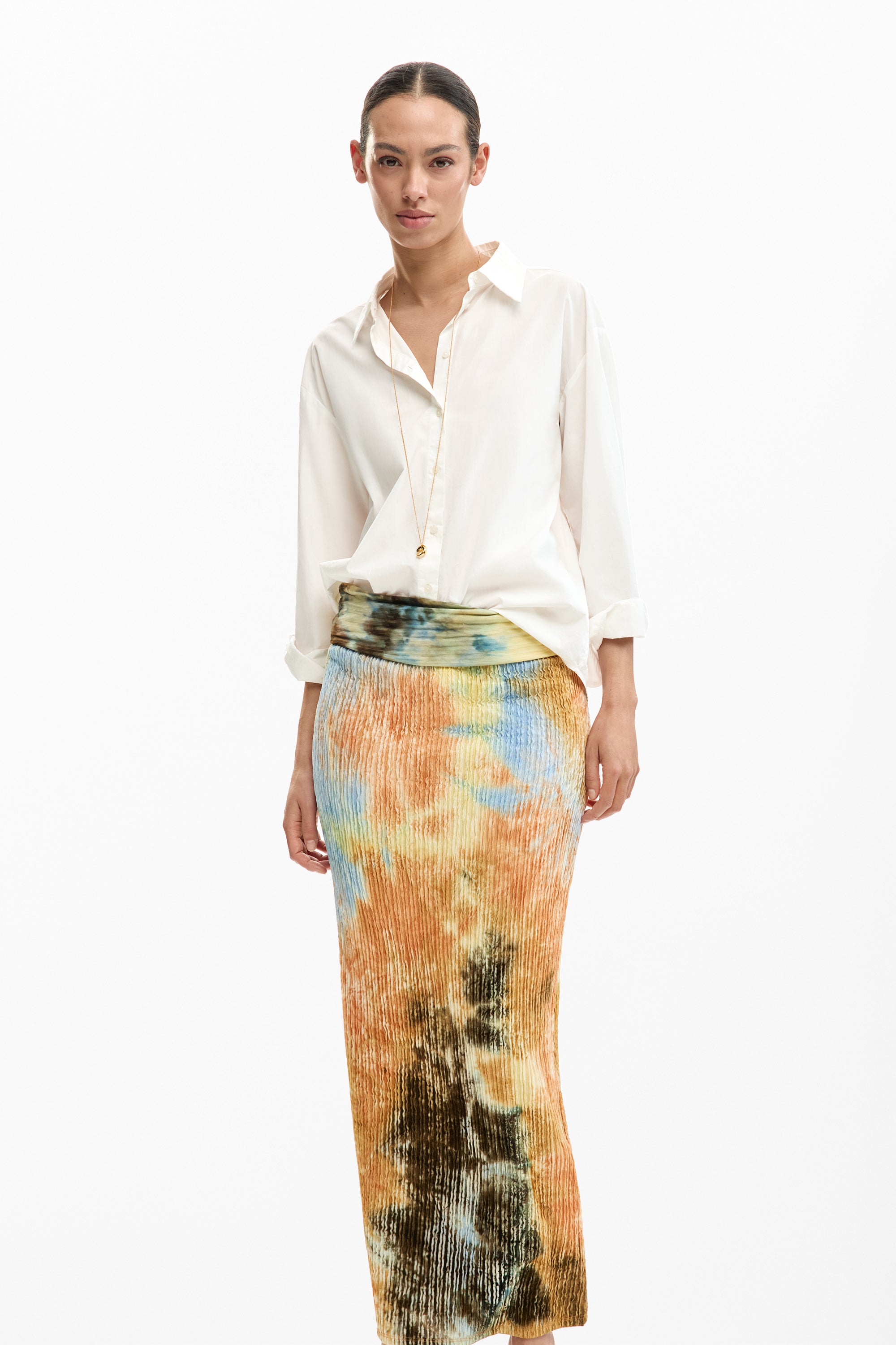 אישה לובשת חצאית פלאיסה צבעונית בגווני כתום וכחול עם חולצה לבנה מכופתרת