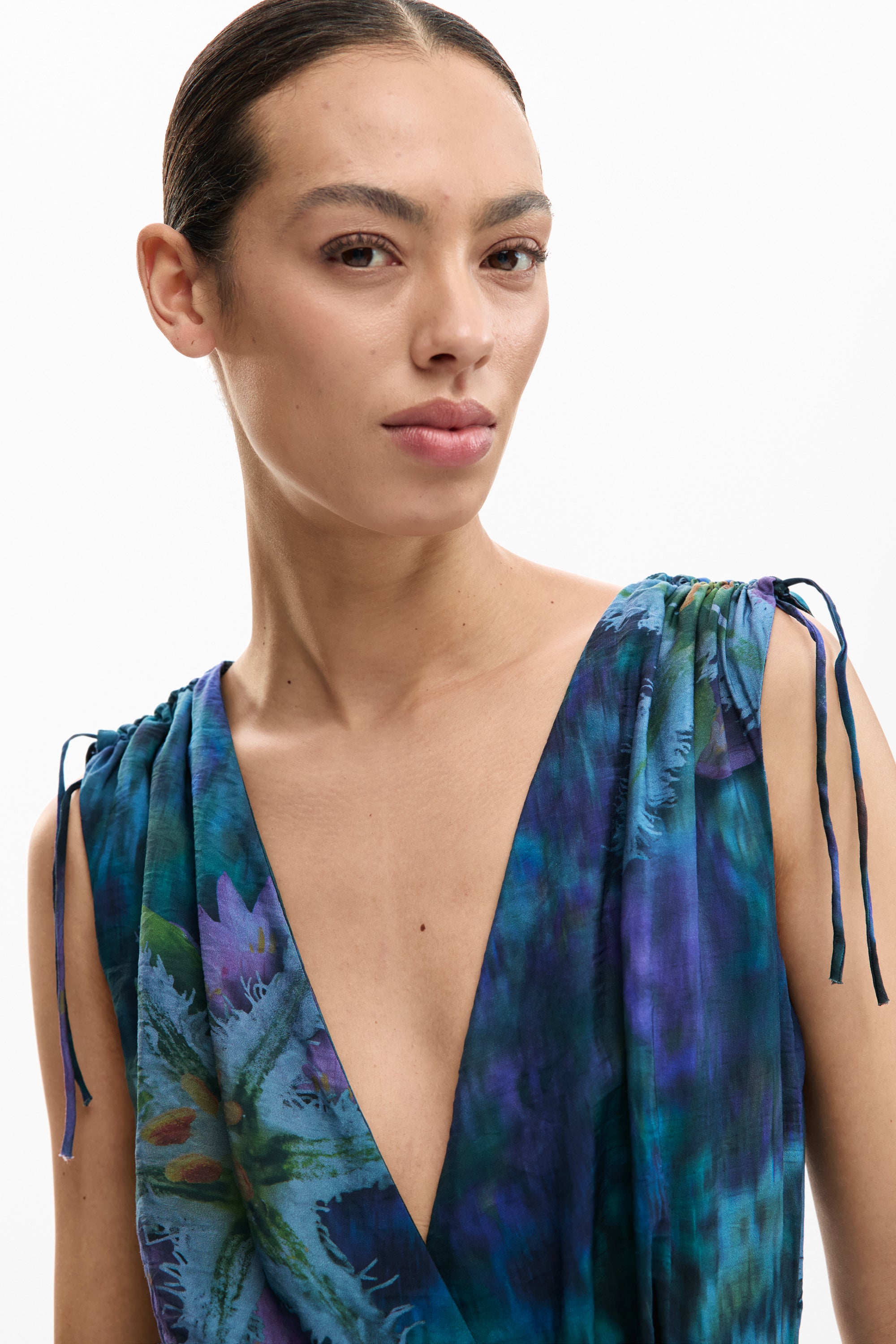 אישה לובשת שמלת וי עמוקה בצבעי כחול וסגול עם דוגמת פרחים, מראה אופנתי ואלגנטי