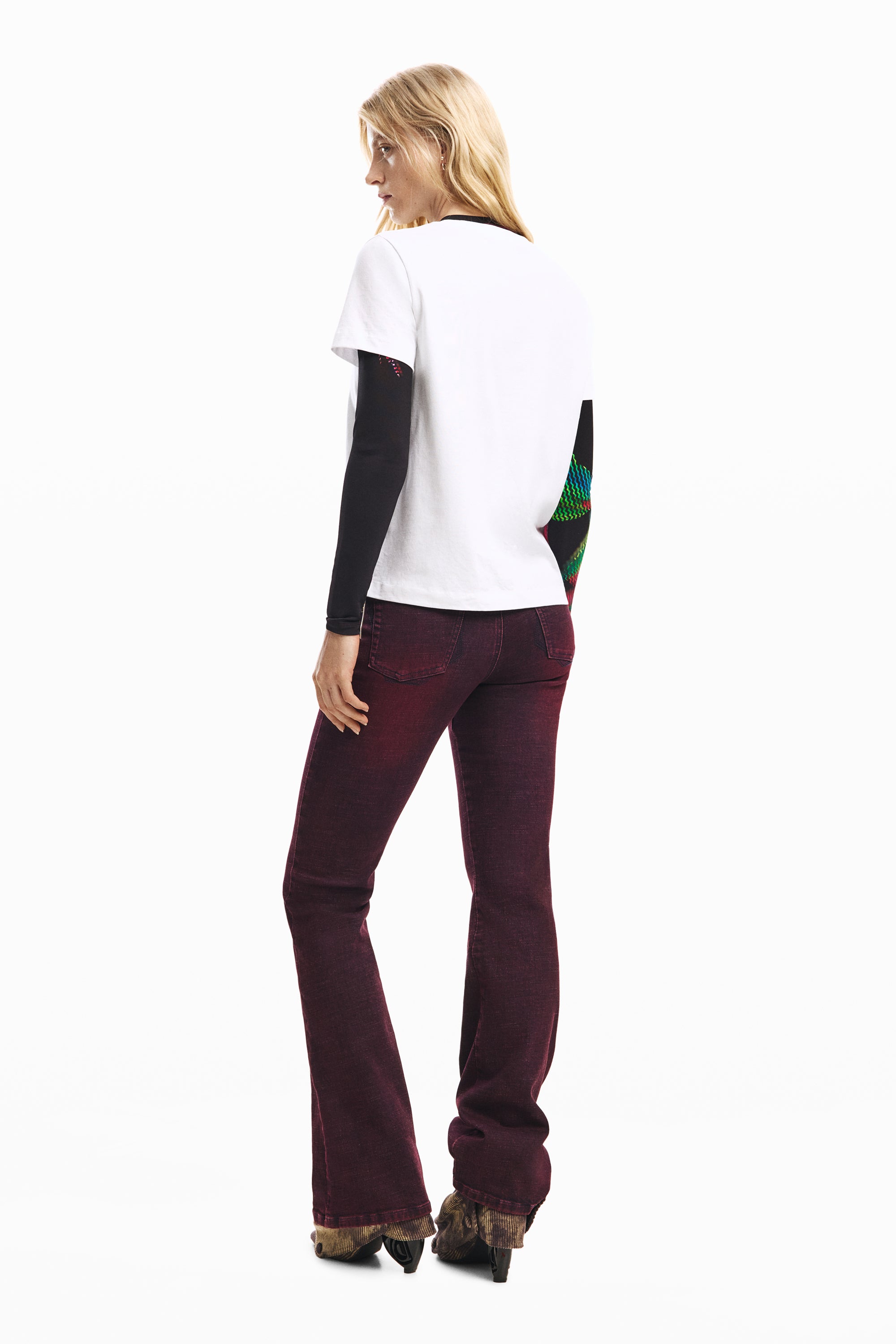 אישה לובשת חולצת טי לבנה עם שרוולים ארוכים שחורים ומכנסי ג'ינס בורדו, צילום מאחור לאופנת נשים