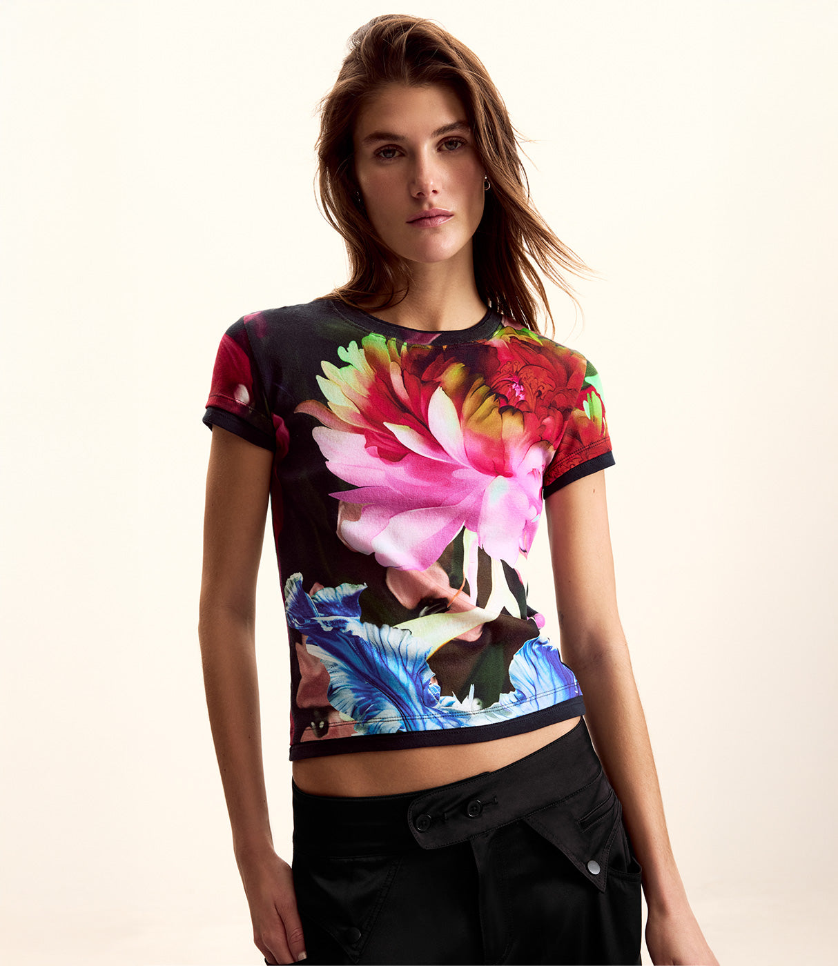 דוגמנית לובשת חולצת טי צבעונית עם הדפסי פרחים גדולים, רקע בהיר, אופנת נשים ססגונית