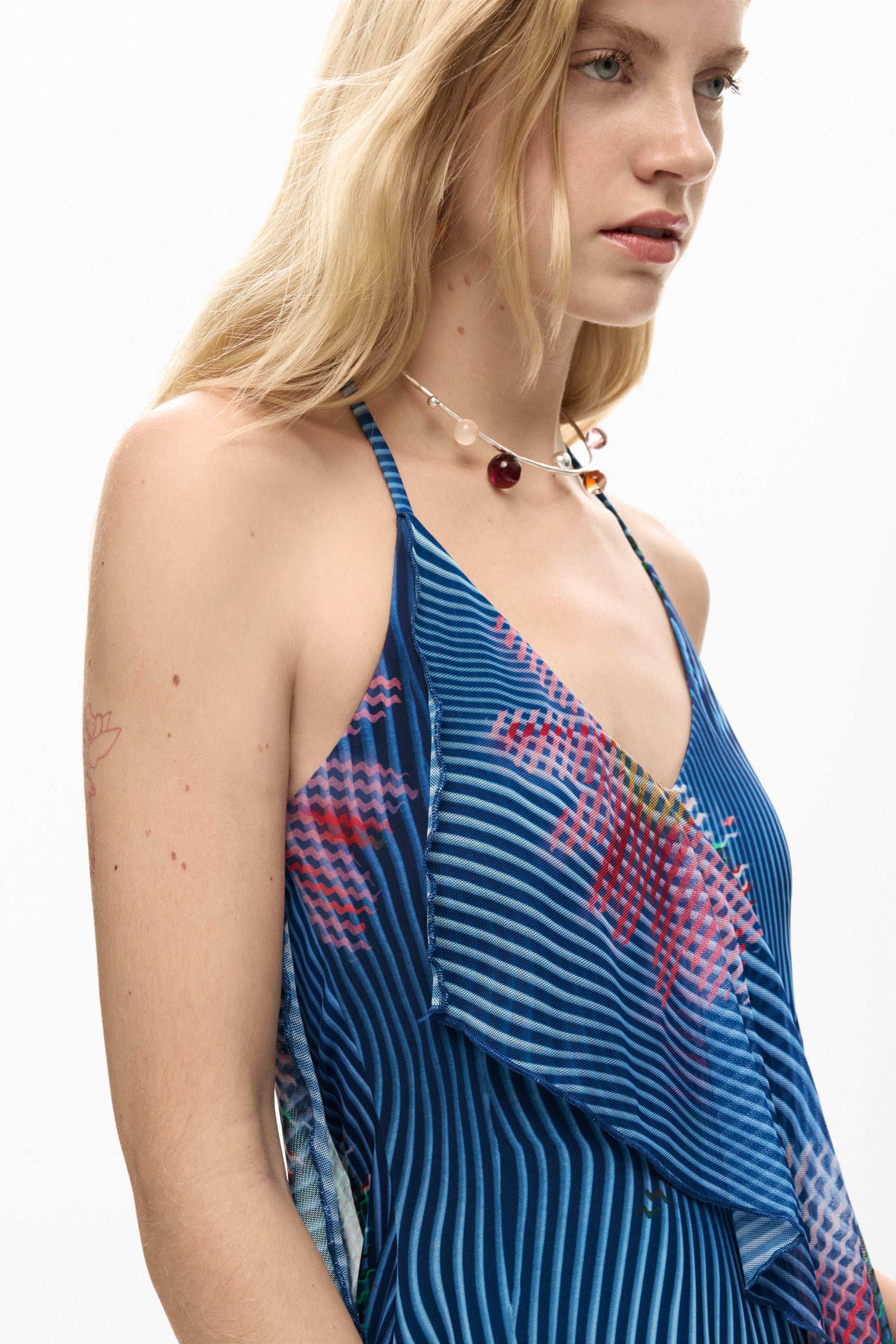 אישה לובשת שמלת קיץ מעבר כחולה עם דוגמת פסים ופרחים, מפתח וי, שרוך צוואר