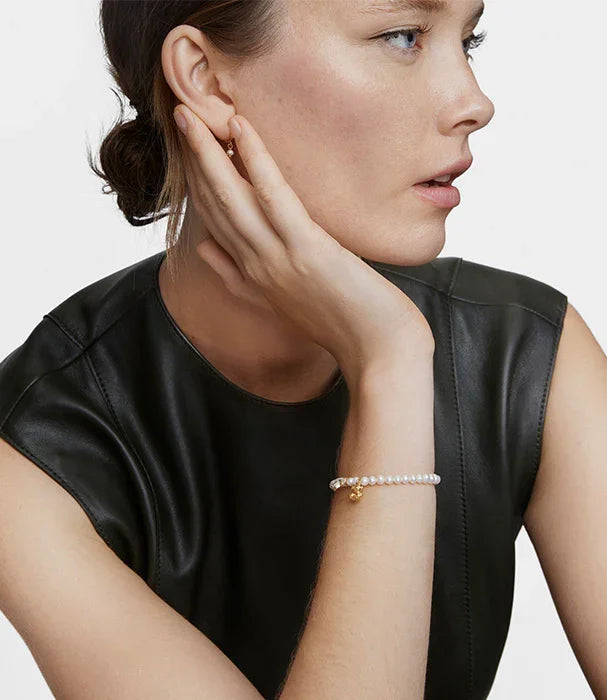 אישה לובשת שמלת עור שחורה, עונדת צמיד פנינים עם תליון זהב, תכשיטים יוקרתיים מבית CHOZEN