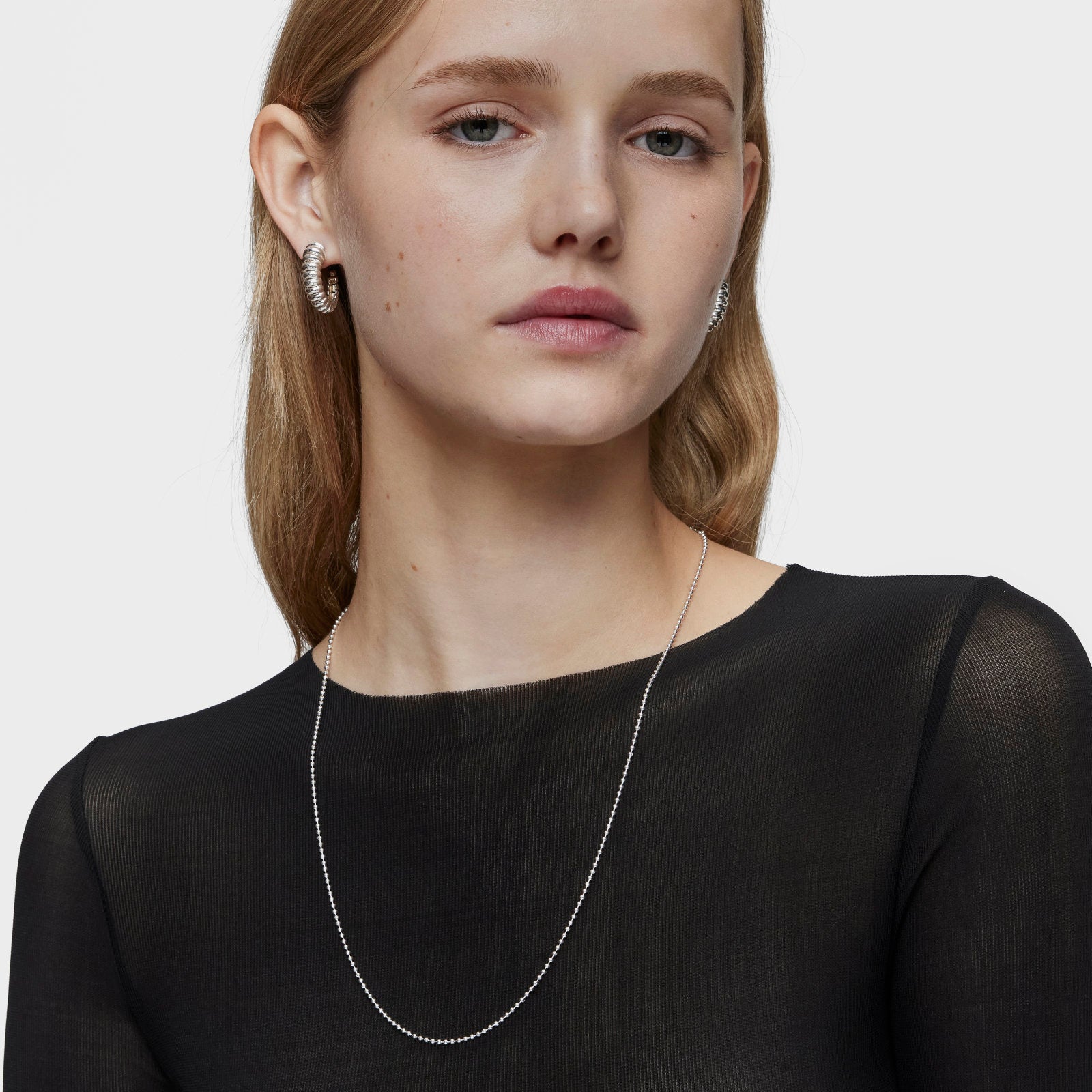 דוגמנית עם עגילי חישוק עבים ותליון כסף דק, חולצה שחורה על רקע לבן