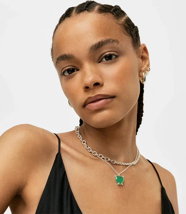 דוגמנית עם שרשרת כסף ותליון ירוק, עגילי זהב, מבט ישיר, ביגוד שחור, רקע לבן - CHOZEN