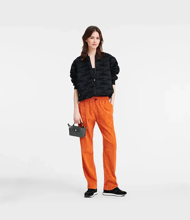 אופנה לנשים CHOZEN: דוגמנית עם ז'קט שחור, מכנסיים כתומים ותיק יד, רקע לבן