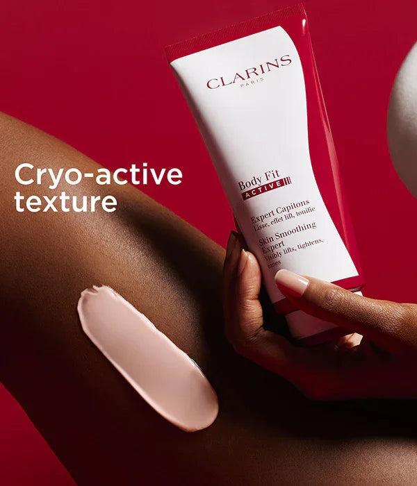 מוצר Clarins Body Fit ACTIVE על עור כהה, טקסטורה קרמית, רקע אדום, מותגים מובילים CHOZEN