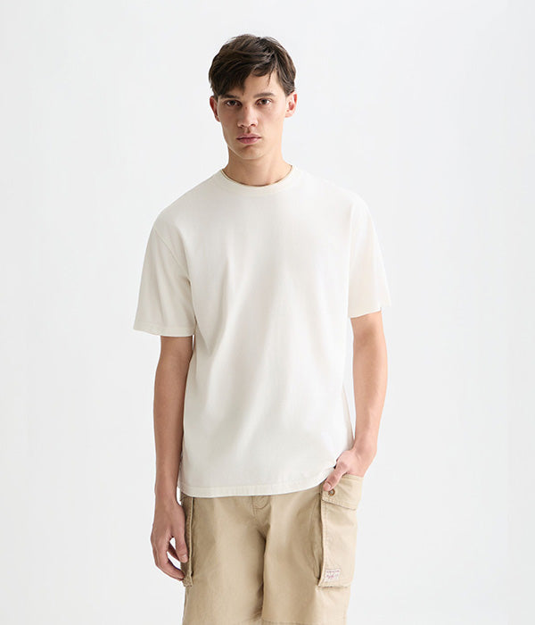 דוגמן לובש חולצת טי לבנה ומכנסיים בז' לצילום אופנה של CHOZEN, רקע לבן נקי