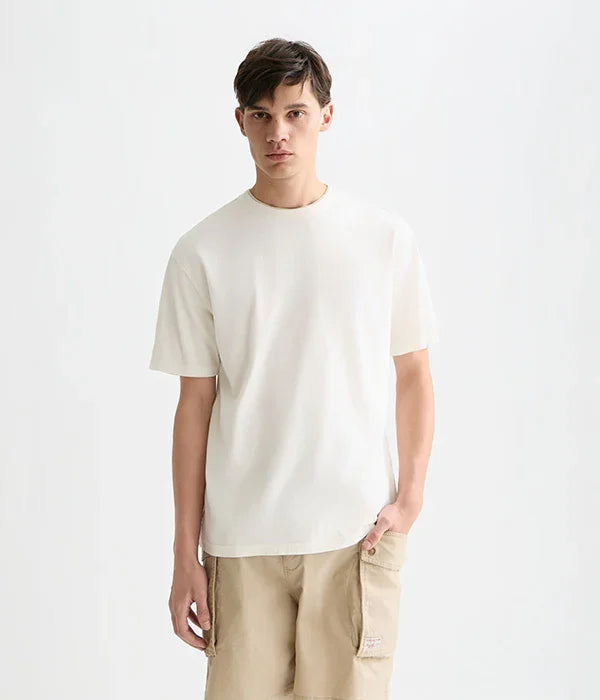 דוגמן לובש חולצת טי לבנה ומכנסיים בז' לצילום אופנה של CHOZEN, רקע לבן נקי