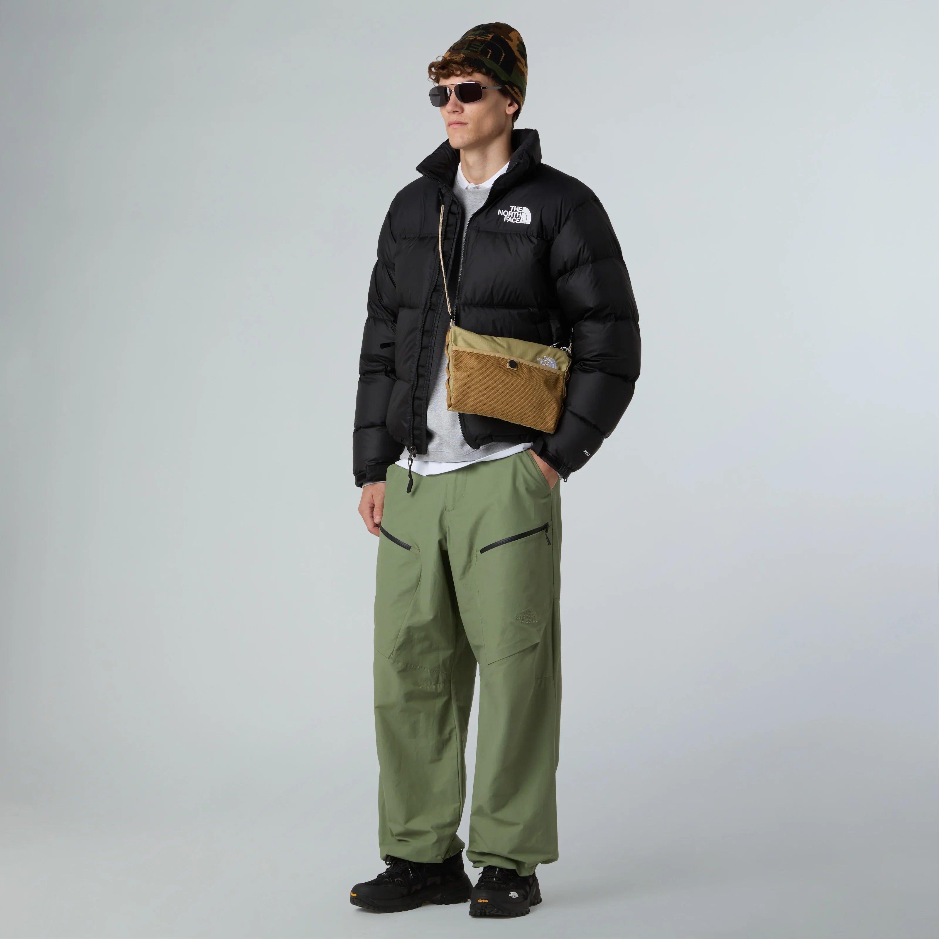 דגם לובש מעיל פוך שחור The North Face, מכנס ירוק, תיק צד חום ומשקפי שמש, צילום אופנה CHOZEN