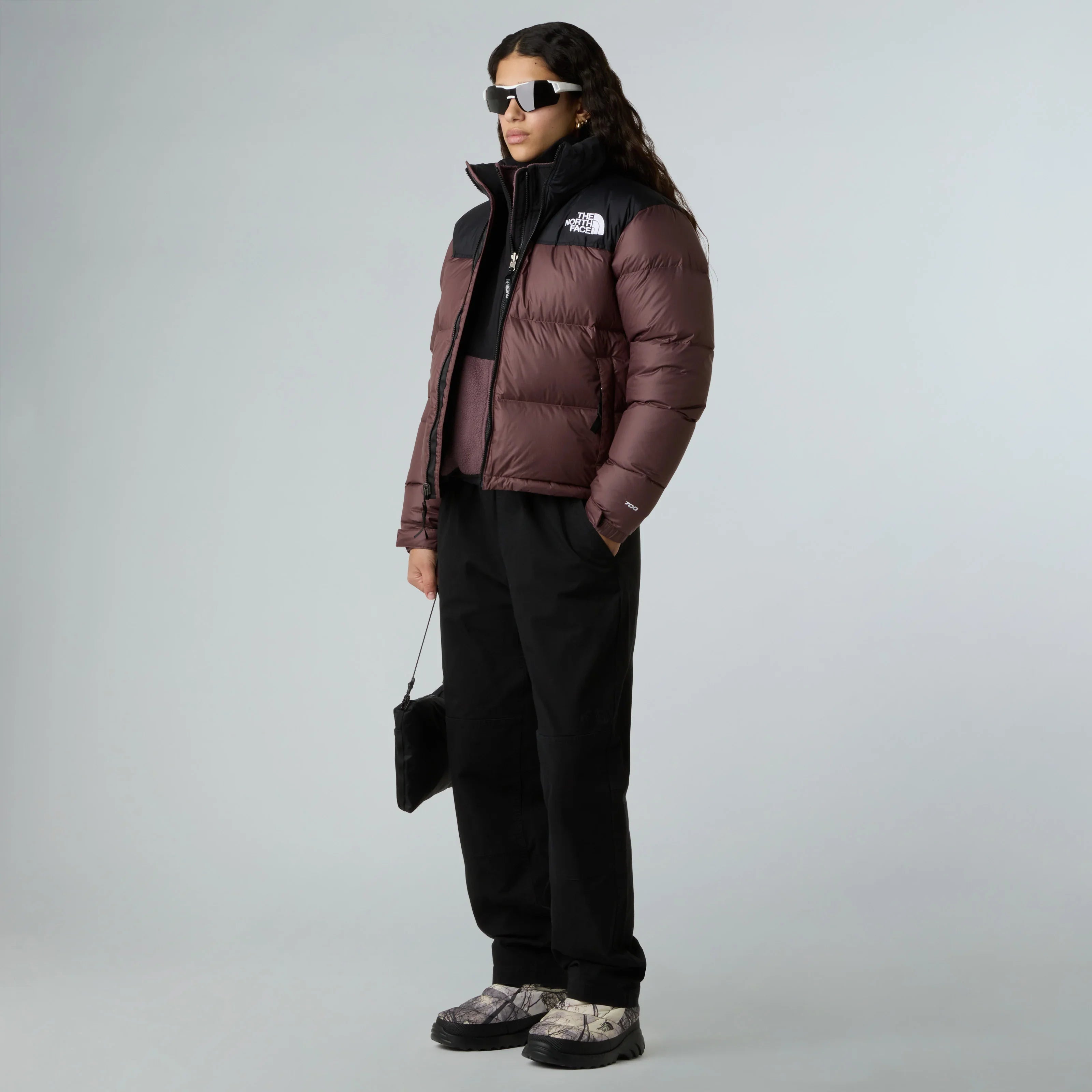 אופנת רחוב: דגם לובש מעיל The North Face חום-שחור, מכנסיים שחורים ונעלי סניקרס, משקפי שמש