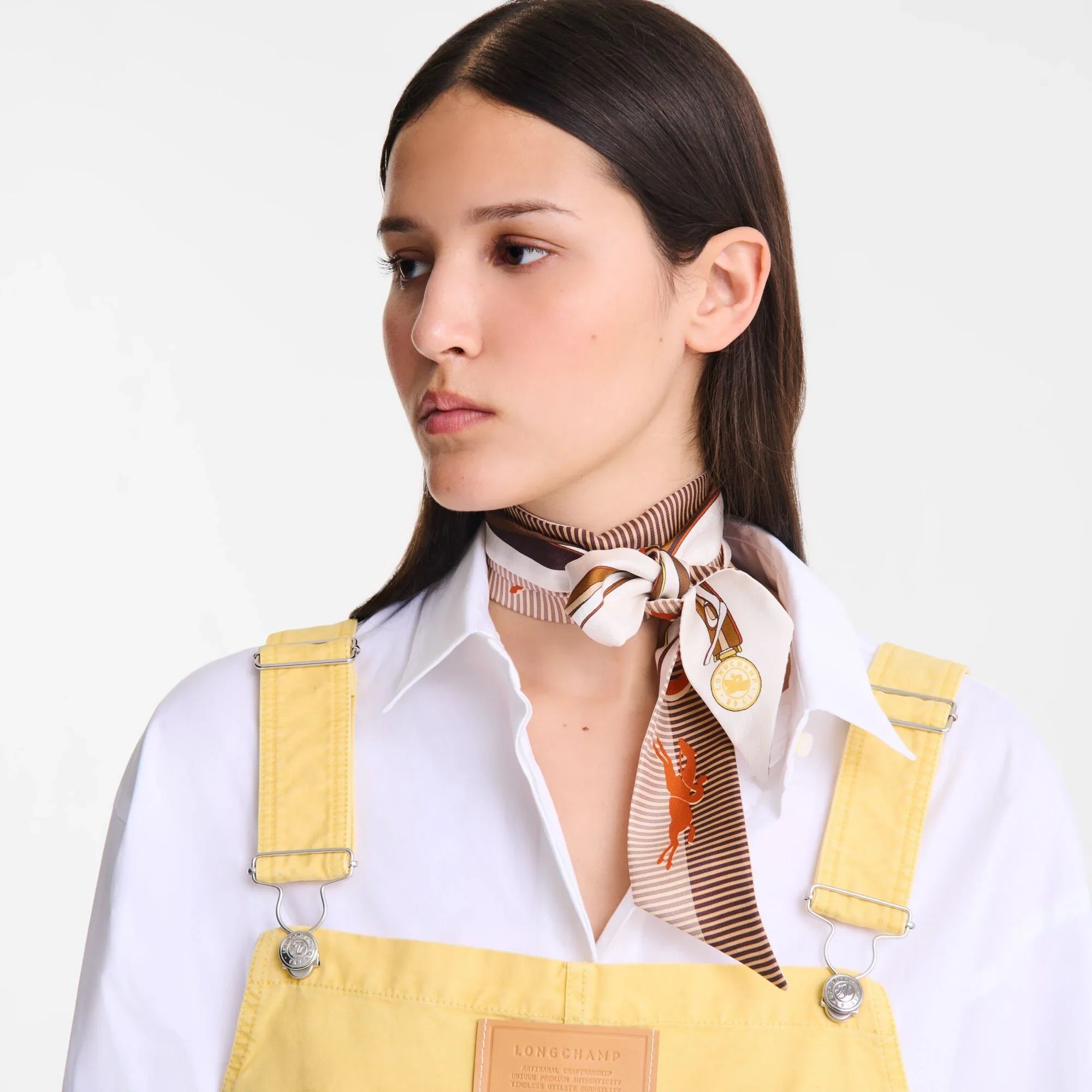 אישה צעירה לובשת חולצה לבנה וסרבל צהוב, צעיף משי אופנתי של LONGCHAMP על צווארה, אופנה CHOZEN