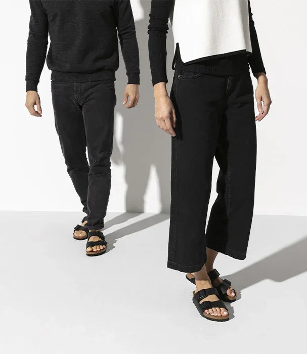 גבר ואישה בוחולצות כהות ומכנסיים שחורות, נועלים סנדלים שחורות, רקע לבן, אופנה CHOZEN