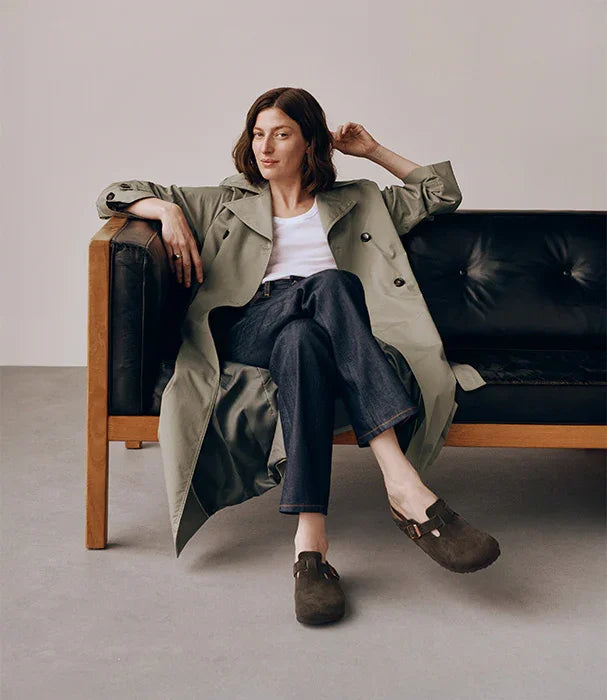 אישה יושבת על ספה, לובשת טרנצ' מעיל, ג'ינס ונעליים חומות, צילום אווירה אופנתי באתר CHOZEN