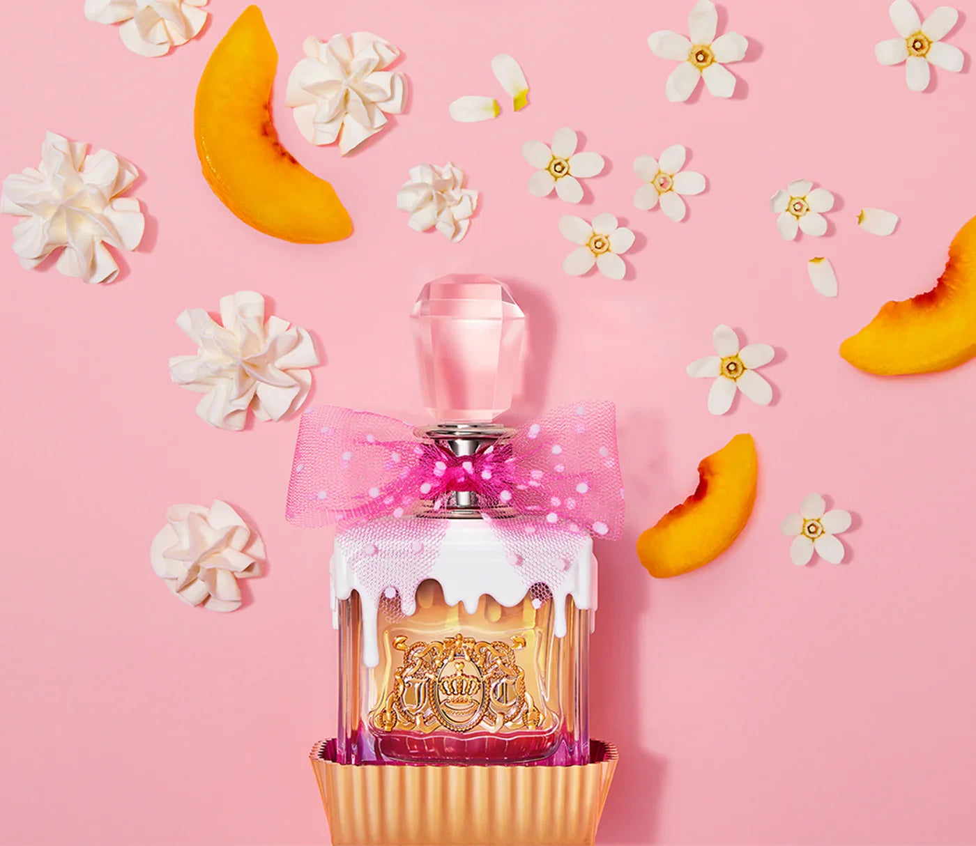 בקבוק בושם מעוצב עם פקק גביש, סרט ורוד, פרחים, קצפת ופלחי אפרסק ברקע ורוד