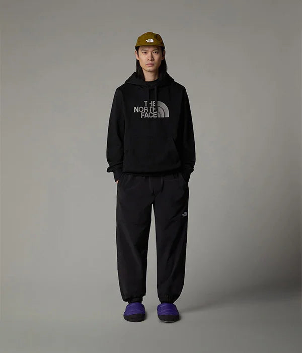 דגם לובש קפוצ'ון שחור של The North Face, מכנסיים שחורים, כובע חום ונעלי בית סגולות, אופנת רחוב מותג CHOZEN