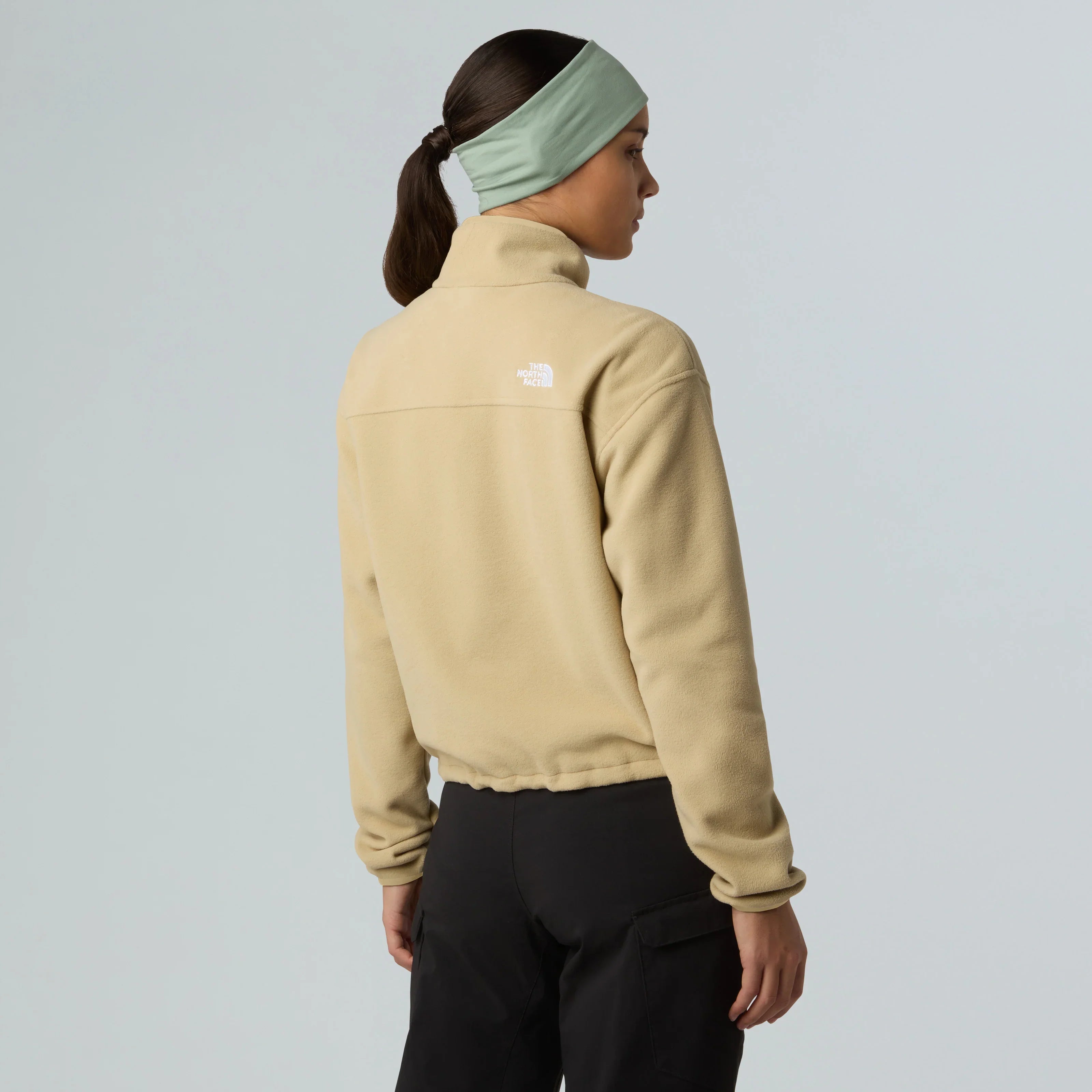 אישה עם פליז The North Face בז׳ ומכנסיים שחורים, על רקע אחיד, מותגים מובילים CHOZEN