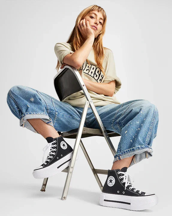 אישה בלבוש קז'ואל יושבת על כיסא, נעלי Converse גבוהות, ג'ינס וחולצת טי, CHOZEN מותגים מובילים