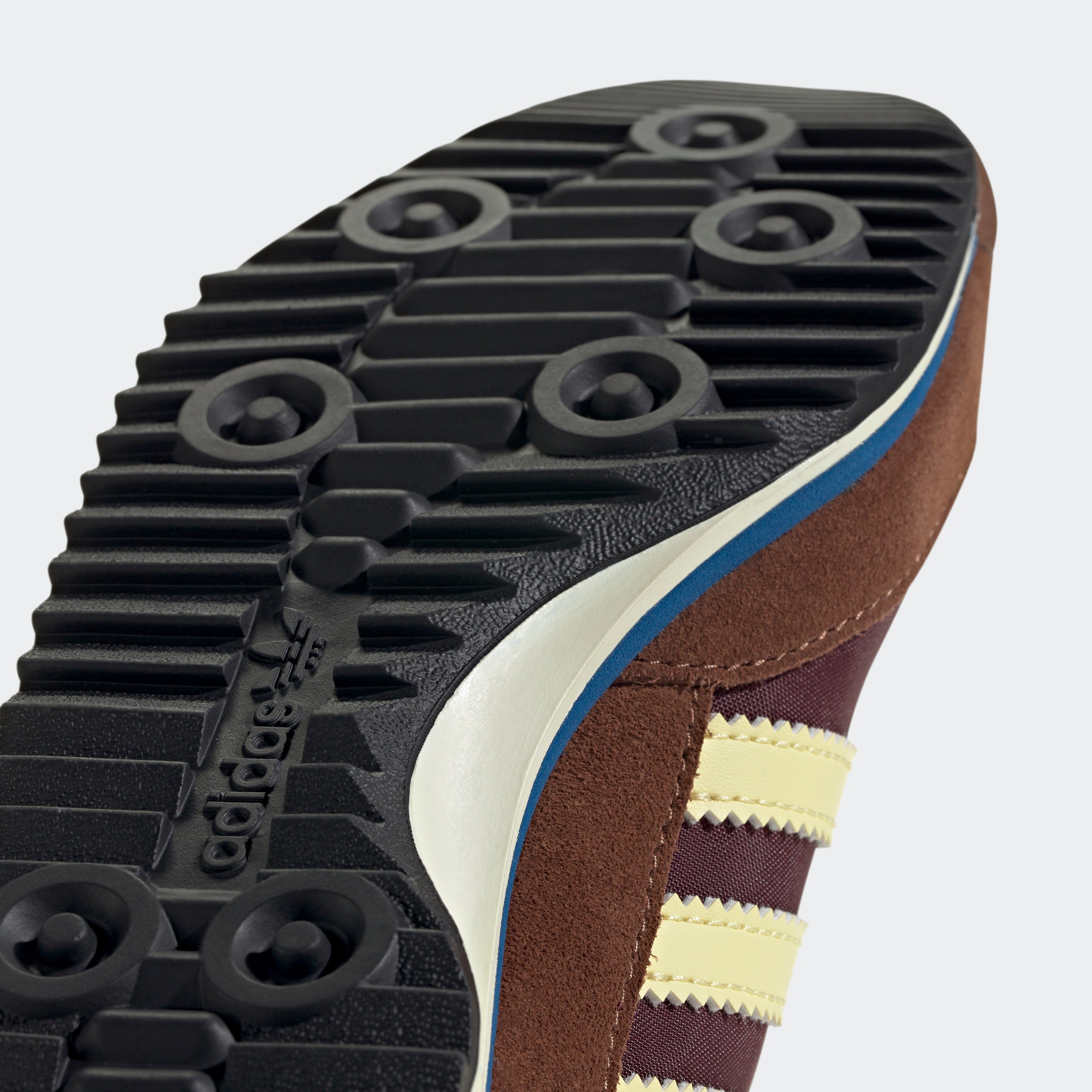 תקריב סוליה של נעל ספורט חומה עם פסים צהובים, גומי מחורץ לאחיזה טובה