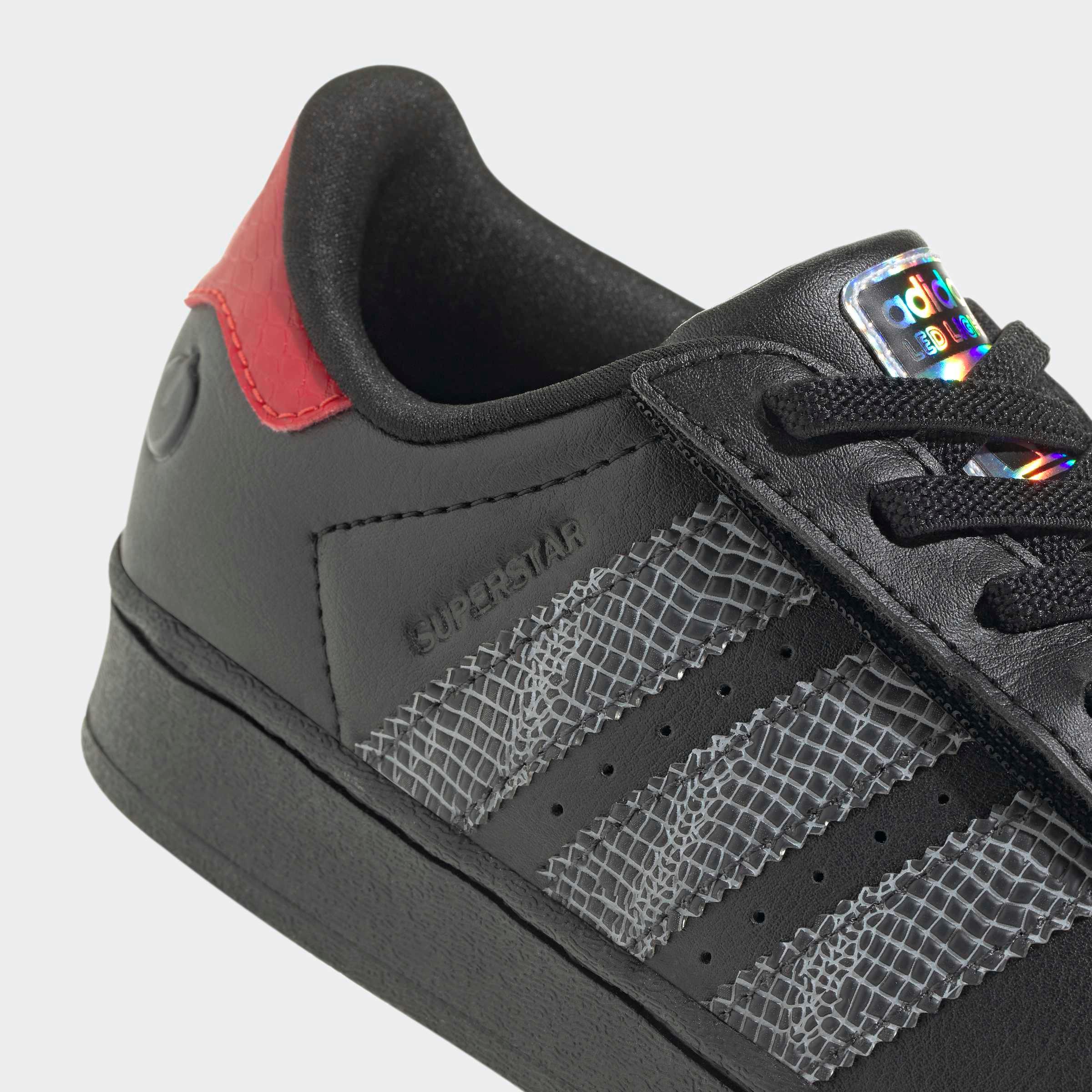 נעל אדידס שחורה עם שלושה פסים אפורים וטקסטורת דמוי נחש, כיתוב SUPERSTAR ועקב אדום