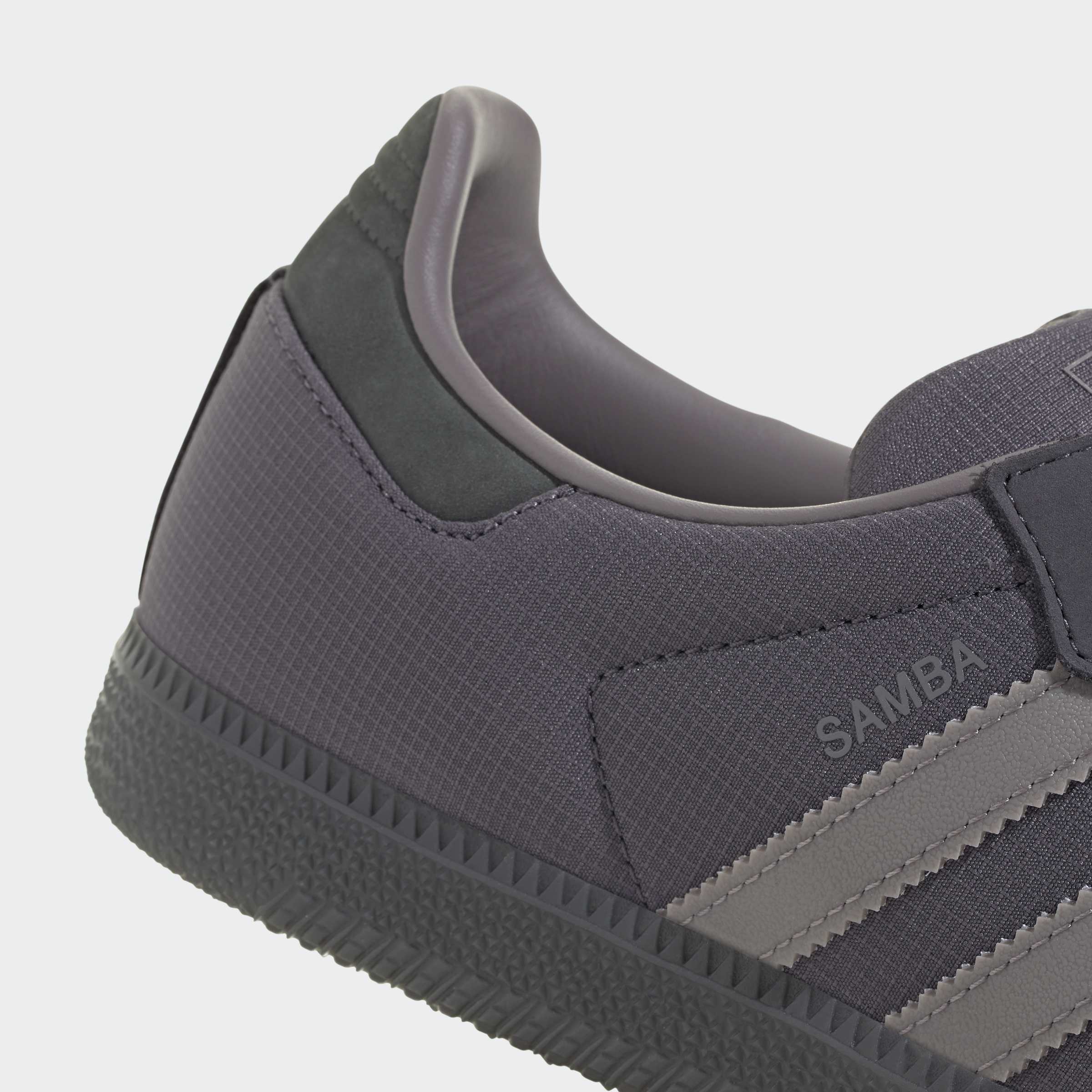 תקריב לנעל ספורט אפורה, עם בד מרקם, כיתוב SAMBA ופסים בצד.