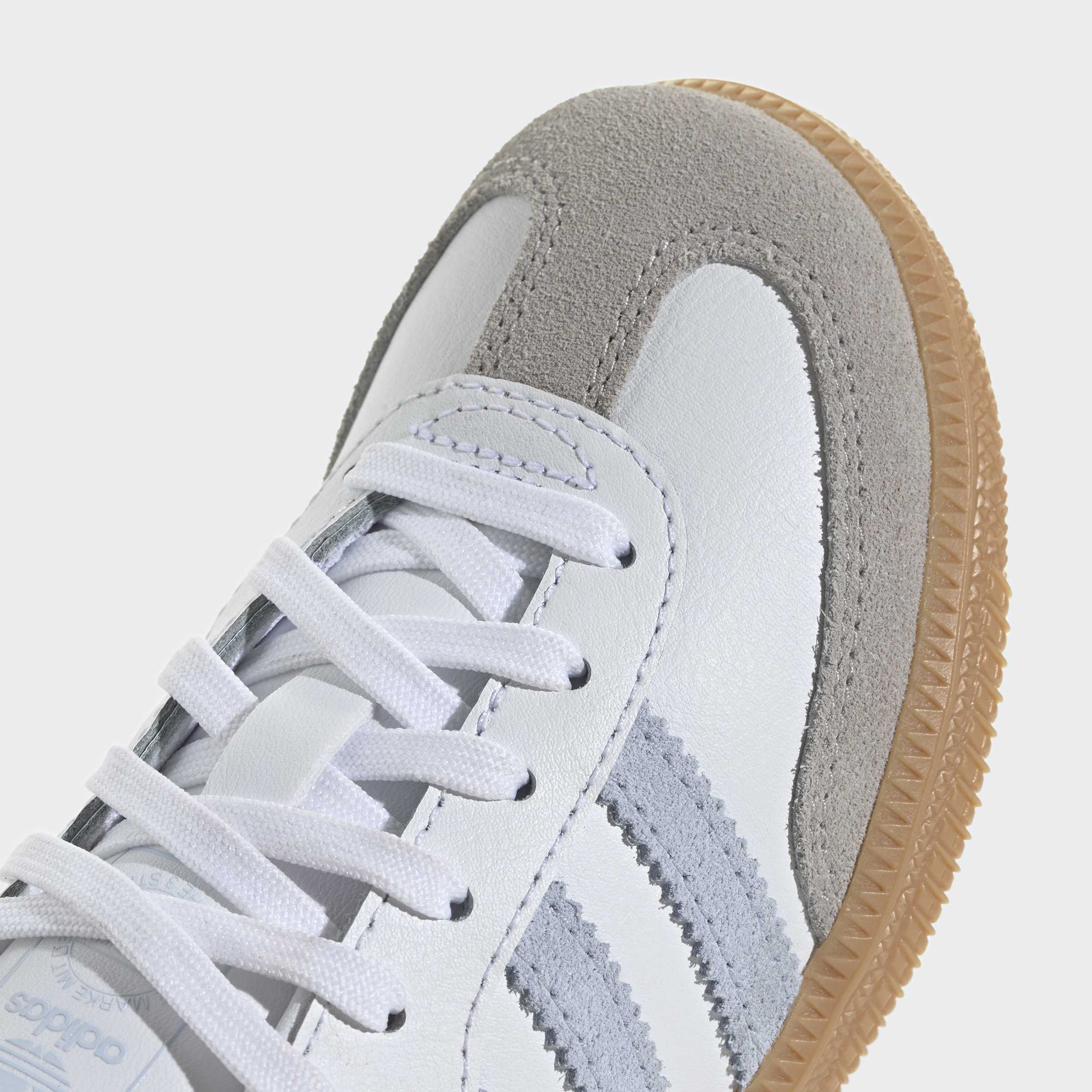 נעל ספורט לבנה עם פסי זמש אפורים וסוליה חומה, תקריב על השרוכים והחלק הקדמי