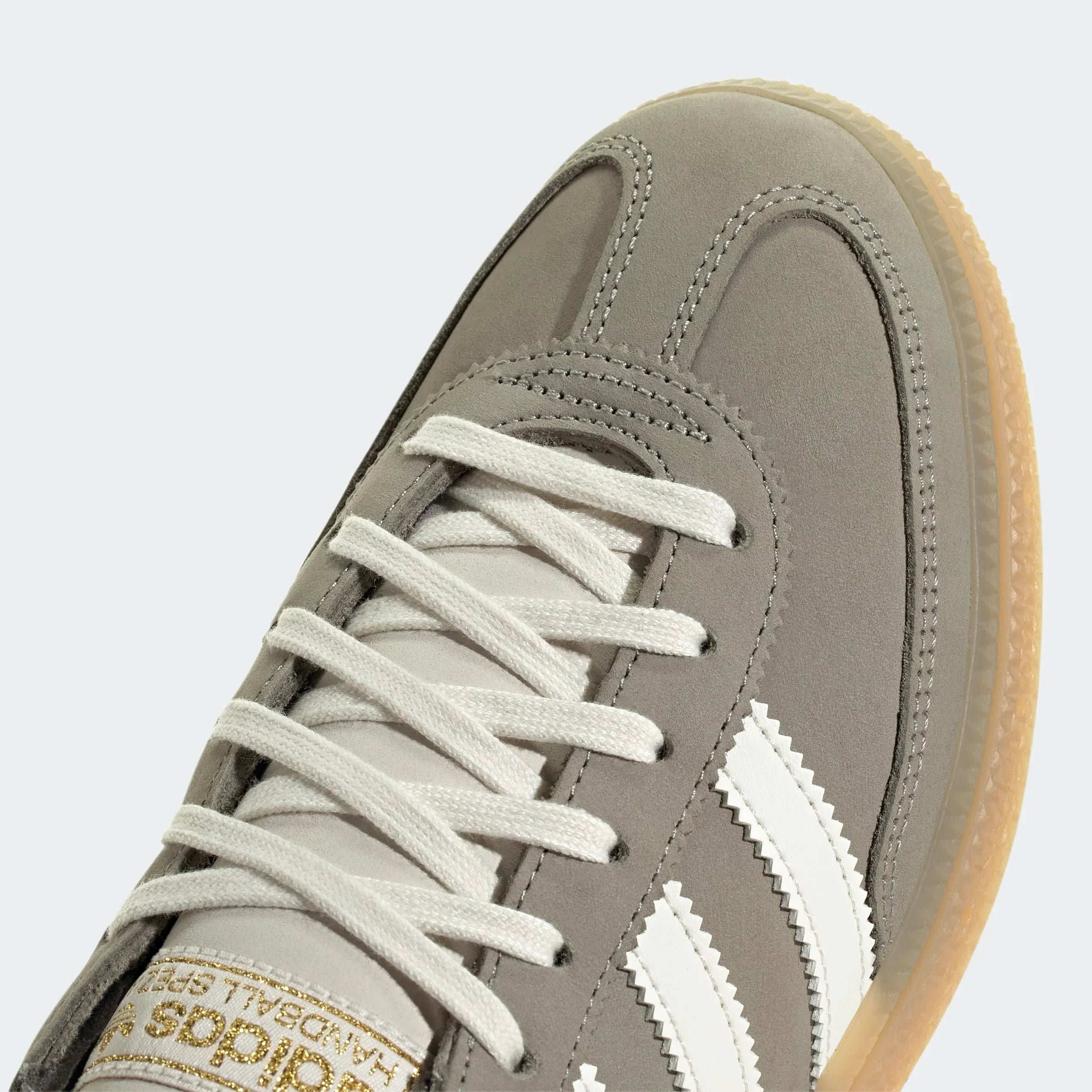 נעל ספורט אפורה עם סוליה בהירה, שרוכים לבנים ושלושה פסים לבנים, צילום תקריב ל-CHOZEN