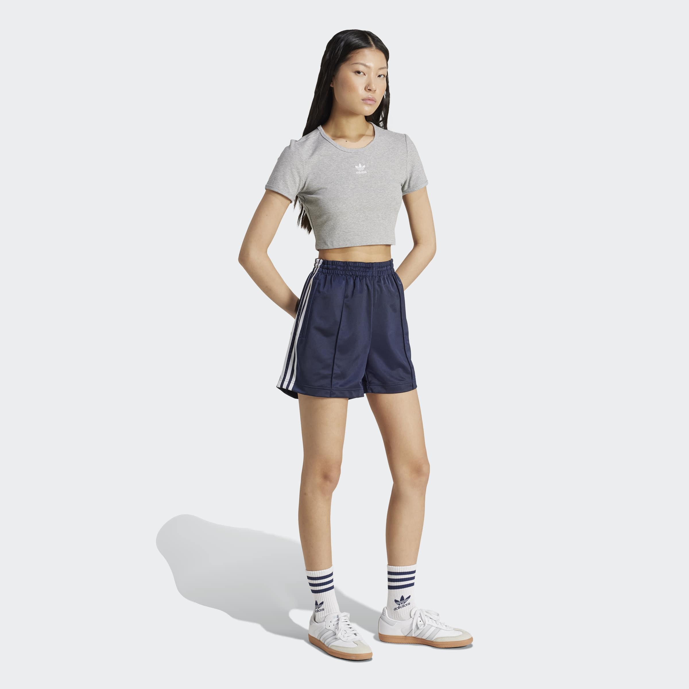 דוגמנית לובשת טופ אפור קצר ומכנסי ספורט כחולים של אדידס, על רקע לבן, ב-CHOZEN
