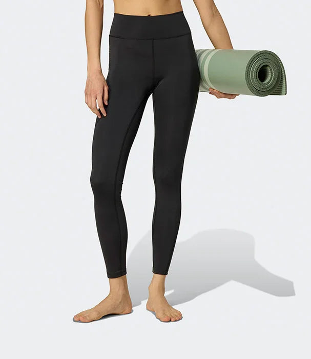 אישה עם טייץ שחור של CHOZEN מחזיקה מזרן יוגה ירוק, לבוש ספורטיבי