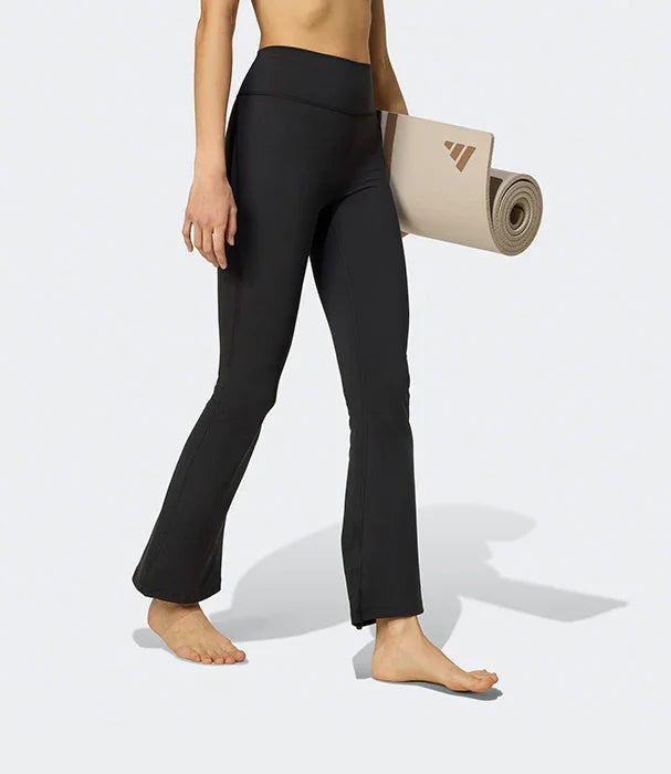 אישה עם מכנסי יוגה שחורים מחטבים, מחזיקה שטיח יוגה, אופנה ספורטיבית CHOZEN