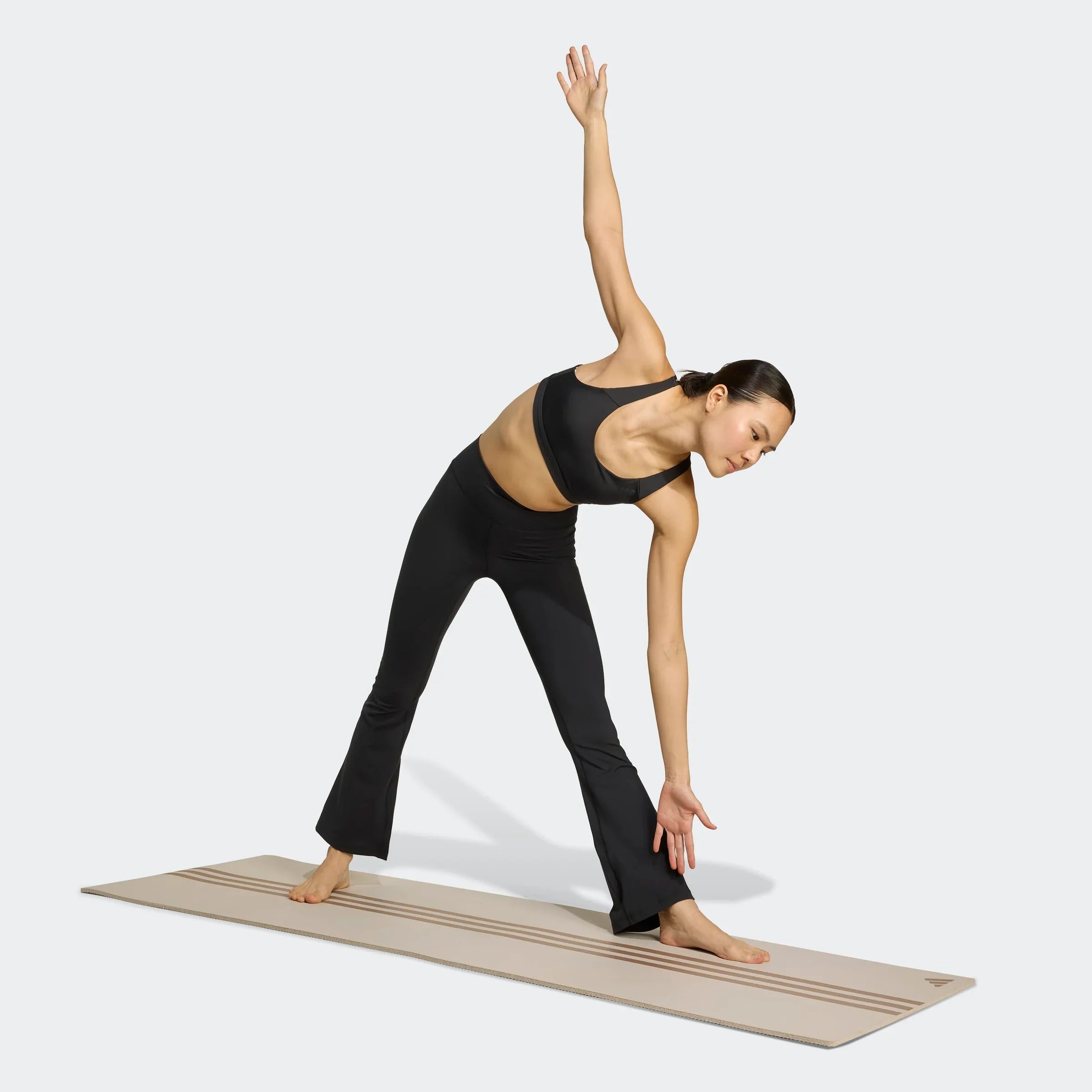אישה בבגדי ספורט שחורים עושה מתיחת יוגה על מזרן, ממותג CHOZEN