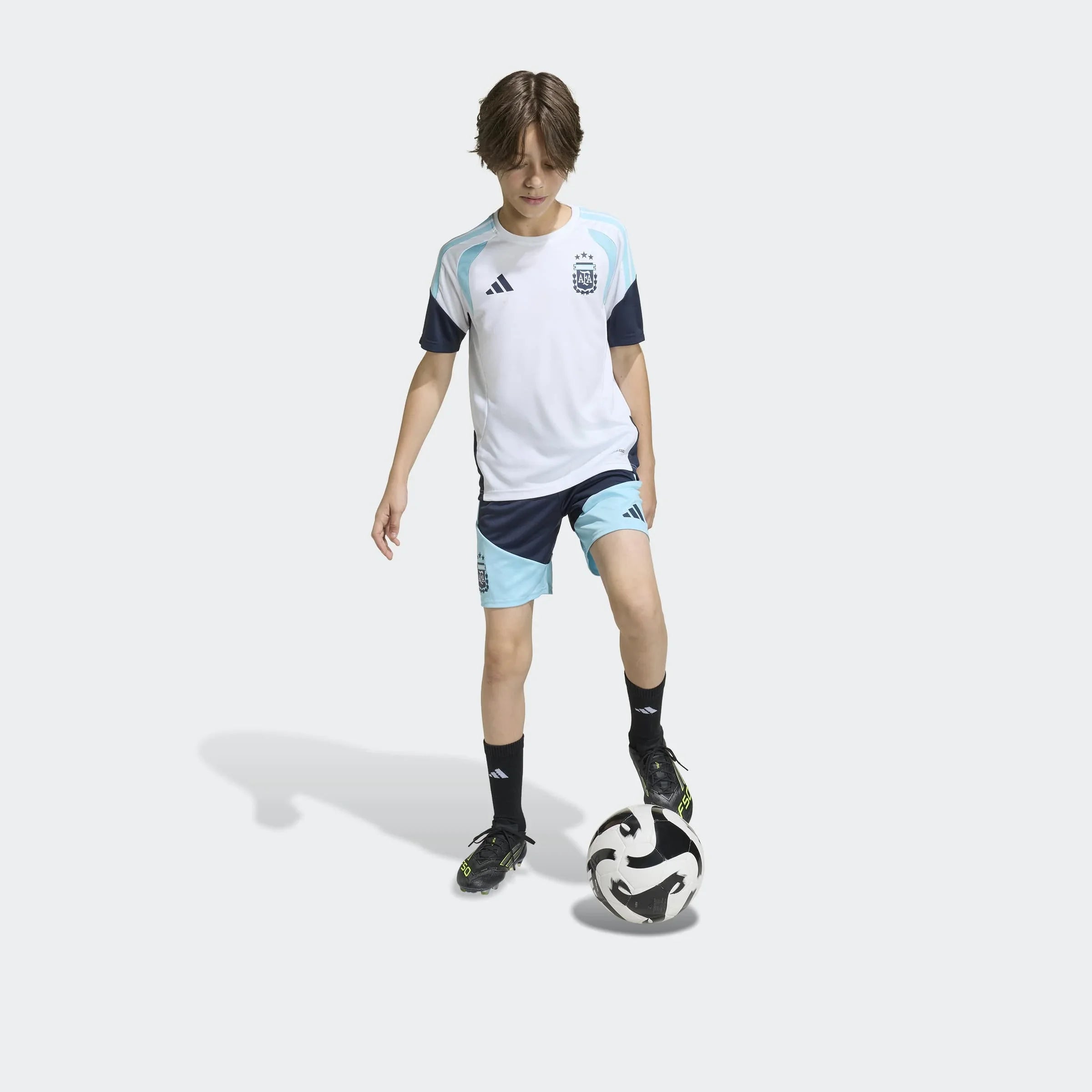 ילד לובש סט כדורגל של אדידס בצבעי תכלת לבן, בועט כדור, רקע אפור, ביגוד ספורט CHOZEN