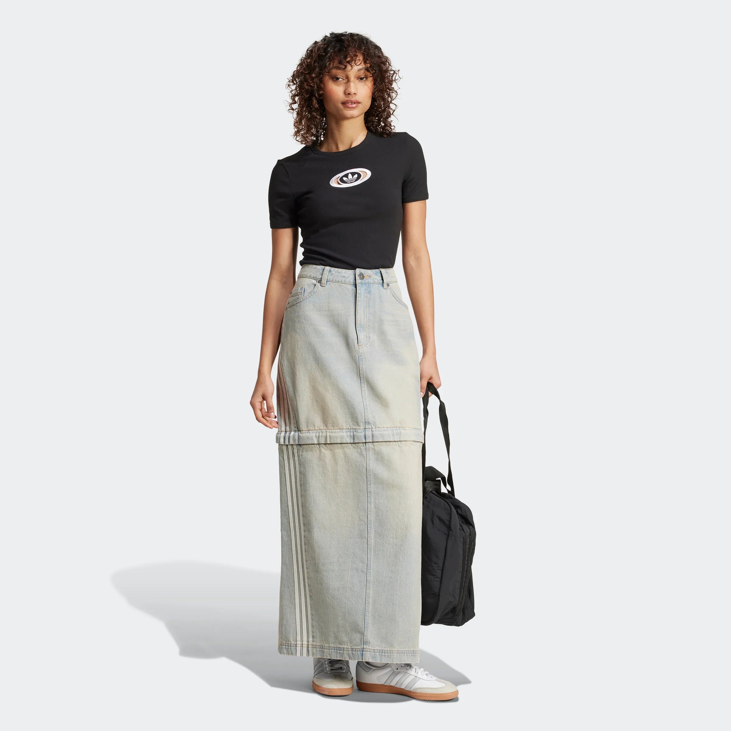 דוגמנית עם חולצה שחורה קצרה של אדידס וחצאית ג'ינס ארוכה בצבע אפור-בהיר, נושאת תיק שחור, צולם על רקע לבן, בקטלוג אופנה של CHOZEN