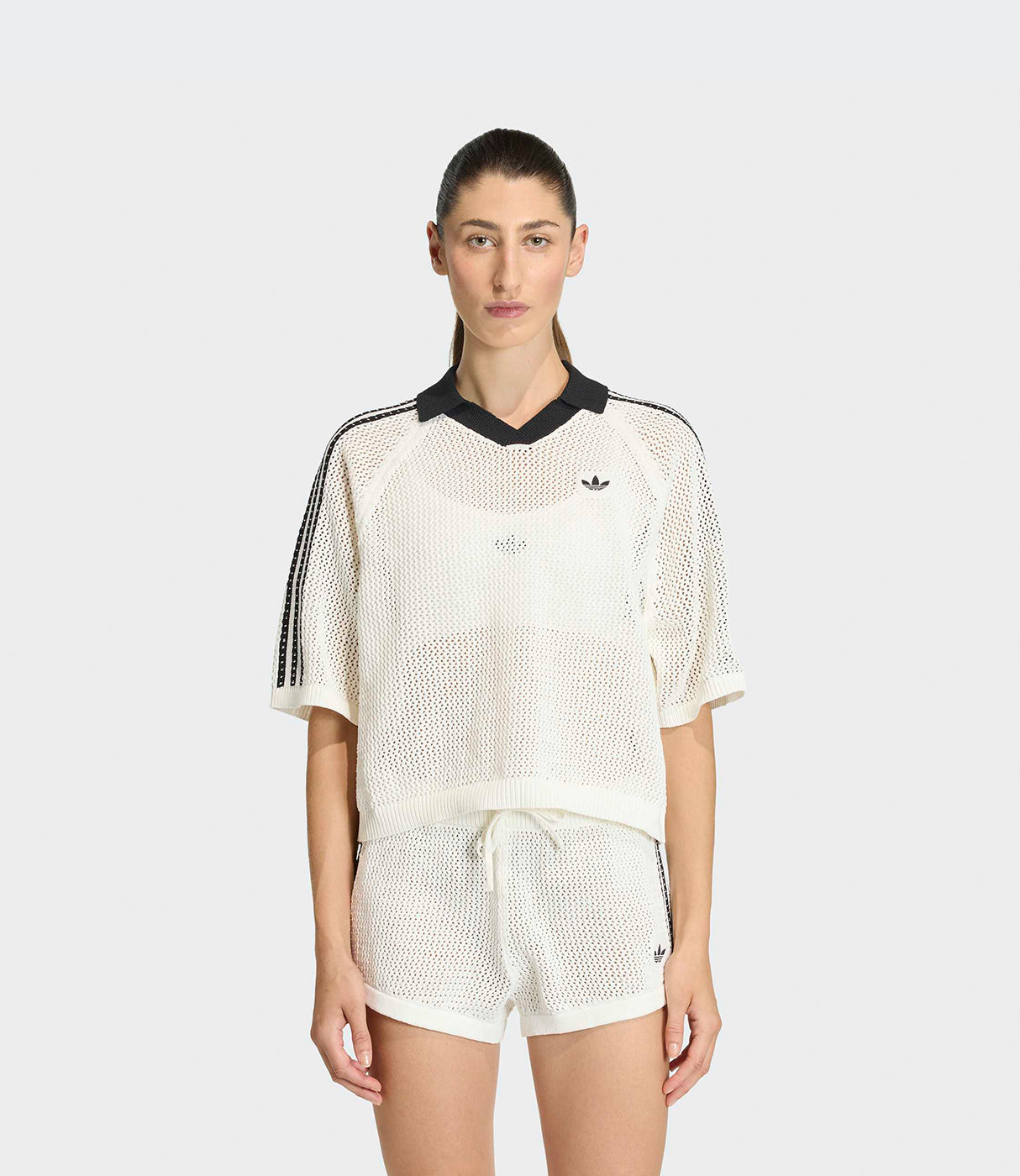 אישה לובשת סט קיץ ספורט רשת לבן עם פסים שחורים, חולצה קצרה ומכנסיים קצרים