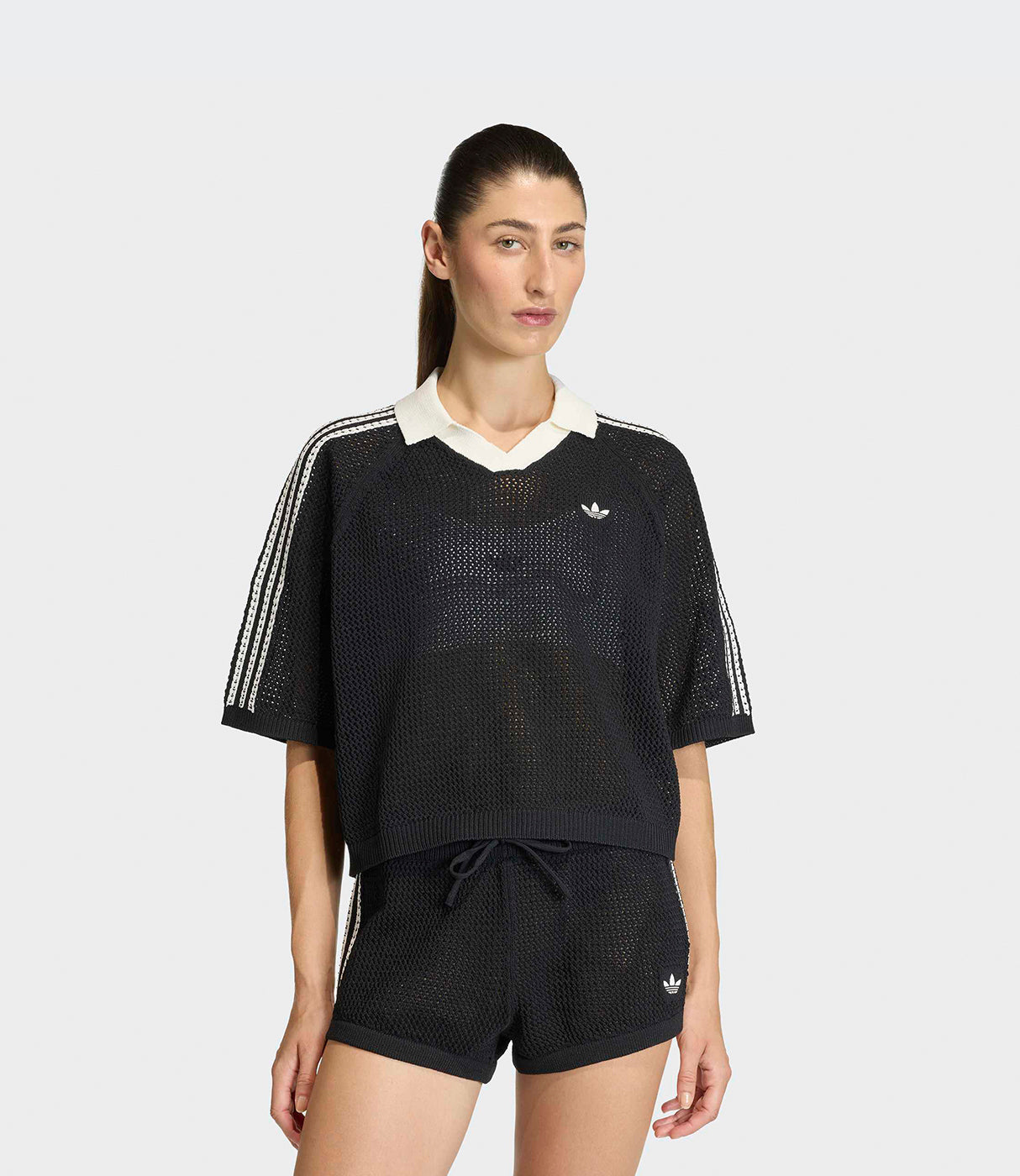 אישה לובשת חולצת רשת שחורה ומכנסיים קצרים תואמים עם פסי ספורט לבנים