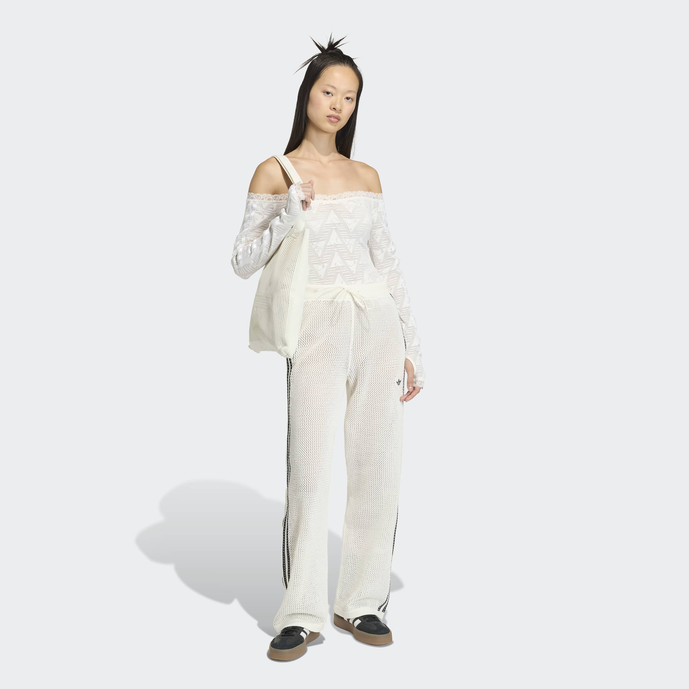 דוגמנית לובשת בגדי אפנה לבנים בסגנון ספורטיבי, מכנסי רשת, חולצה עם כתפיים חשופות ותיק בד