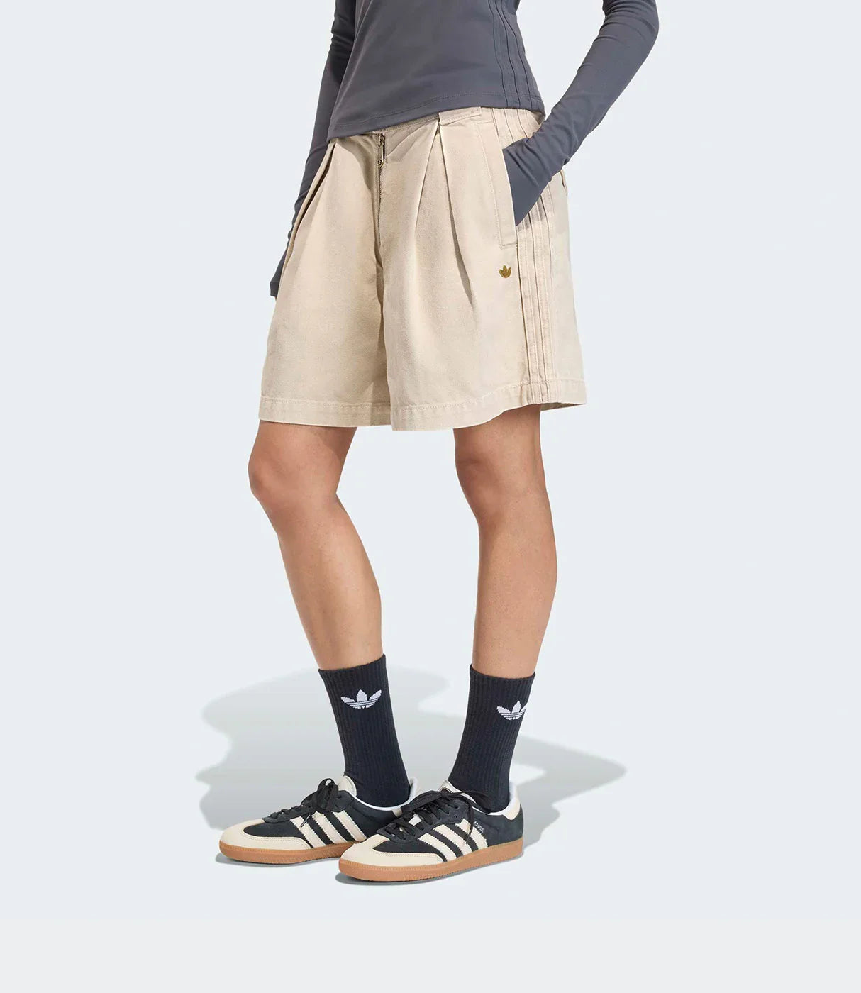 אישה לובשת חולצת שרוול ארוך אפורה, מכנסיים קצרים בז' ונעלי אדידס ספורט עם גרביים שחורות