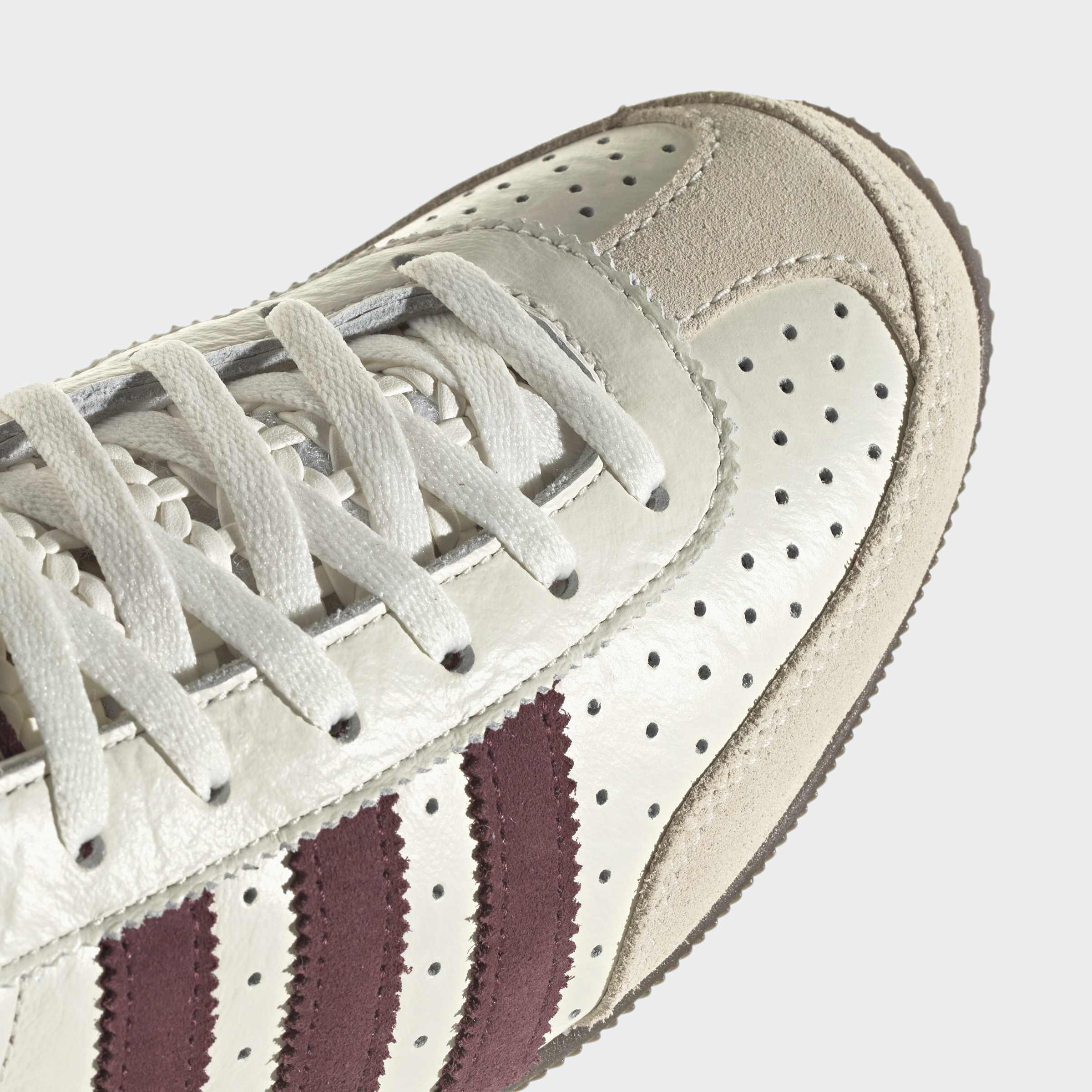 צילום תקריב של נעל ספורט אלגנטית בצבע לבן עם פסים סגולים ועור מחורר