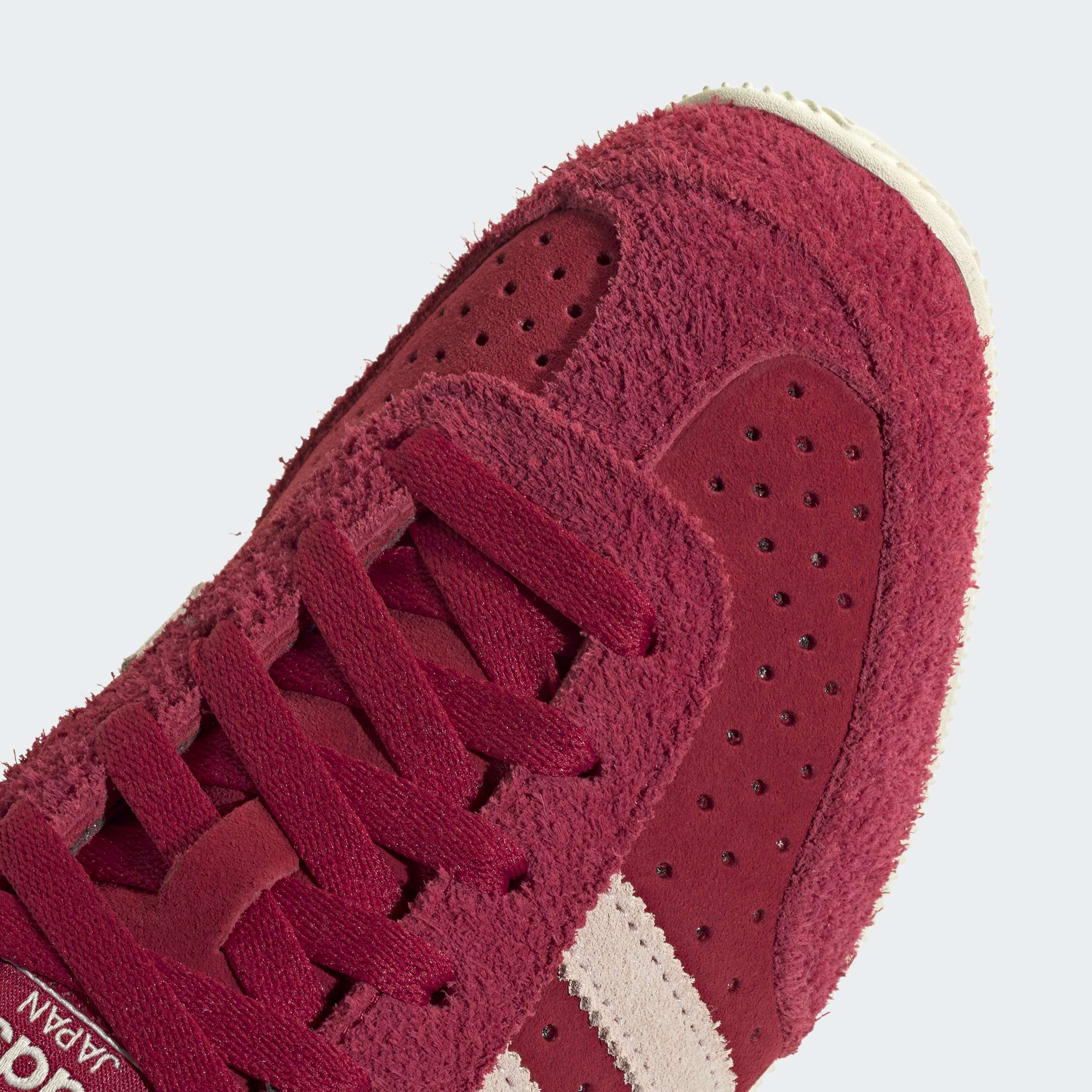 נעל ספורט אדומה עם שרוכים, גפה מזמש מחוספס ופסים לבנים, תקריב על קצה הנעל