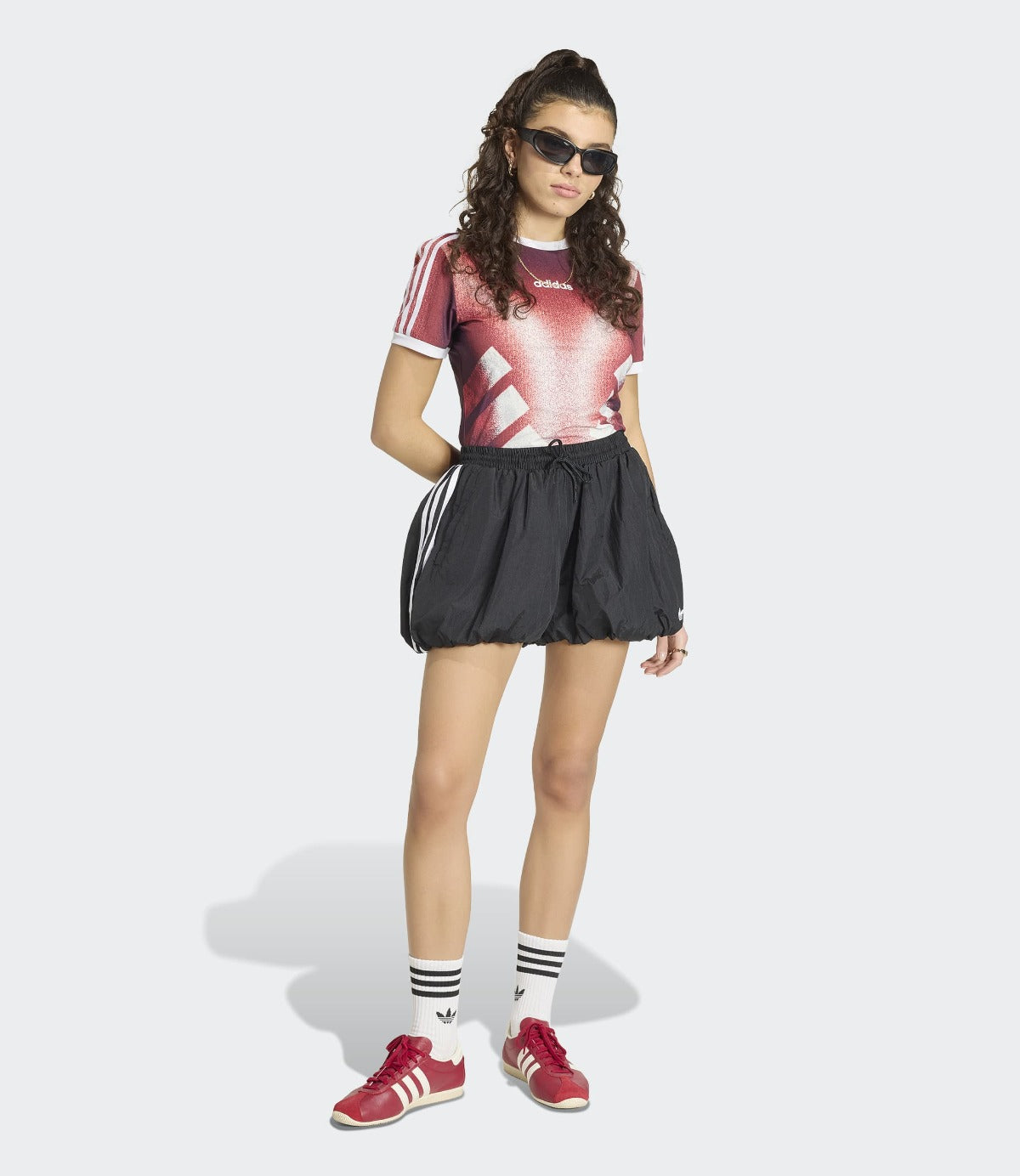 אישה עם חולצת אדום הדפס גרפי, חצאית ספורט שחורה, נעלי ספורט אדומות וגרביים לבנות