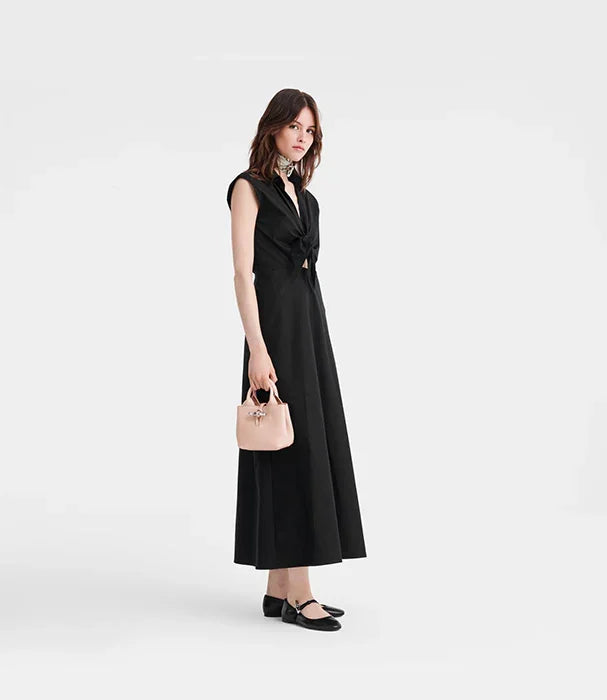 אישה בשמלה שחורה אלגנטית אוחזת תיק קטן, צולמה על רקע לבן, אופנה CHOZEN