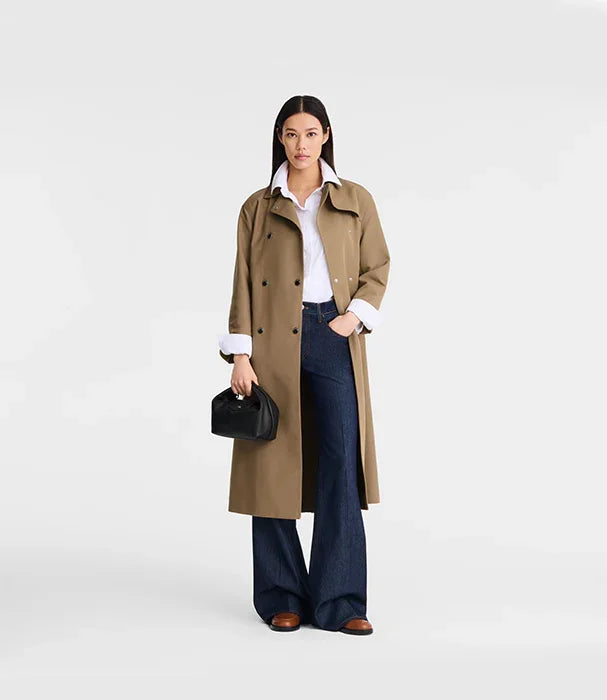 אישה עם מעיל טרנץ' חום, חולצה לבנה ומכנסי ג'ינס כהים, מחזיקה תיק שחור, CHOZEN אופנה מובילה